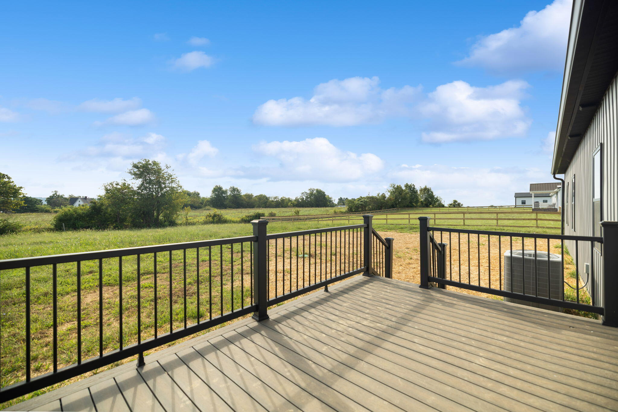 Raised deck with black railings overlooking a fenced grassy field beside the home.