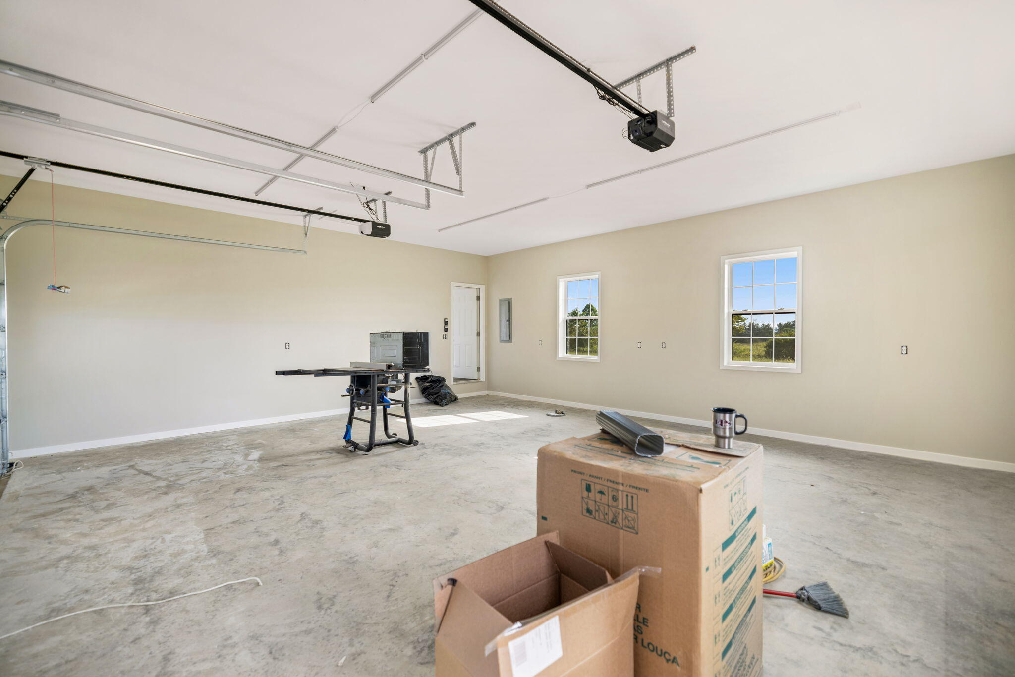 Spacious garage with concrete floors, two windows, overhead door openers, a workbench, and moving boxes.