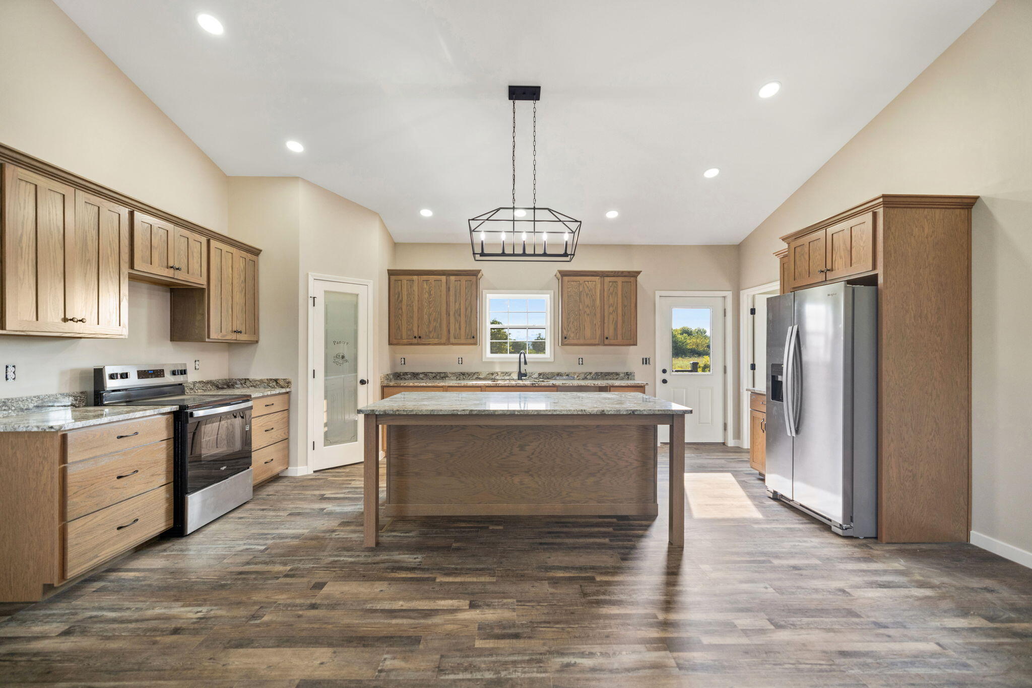 Vacant kitchen with a large stone-topped island, warm wood cabinets, and stainless steel appliances.