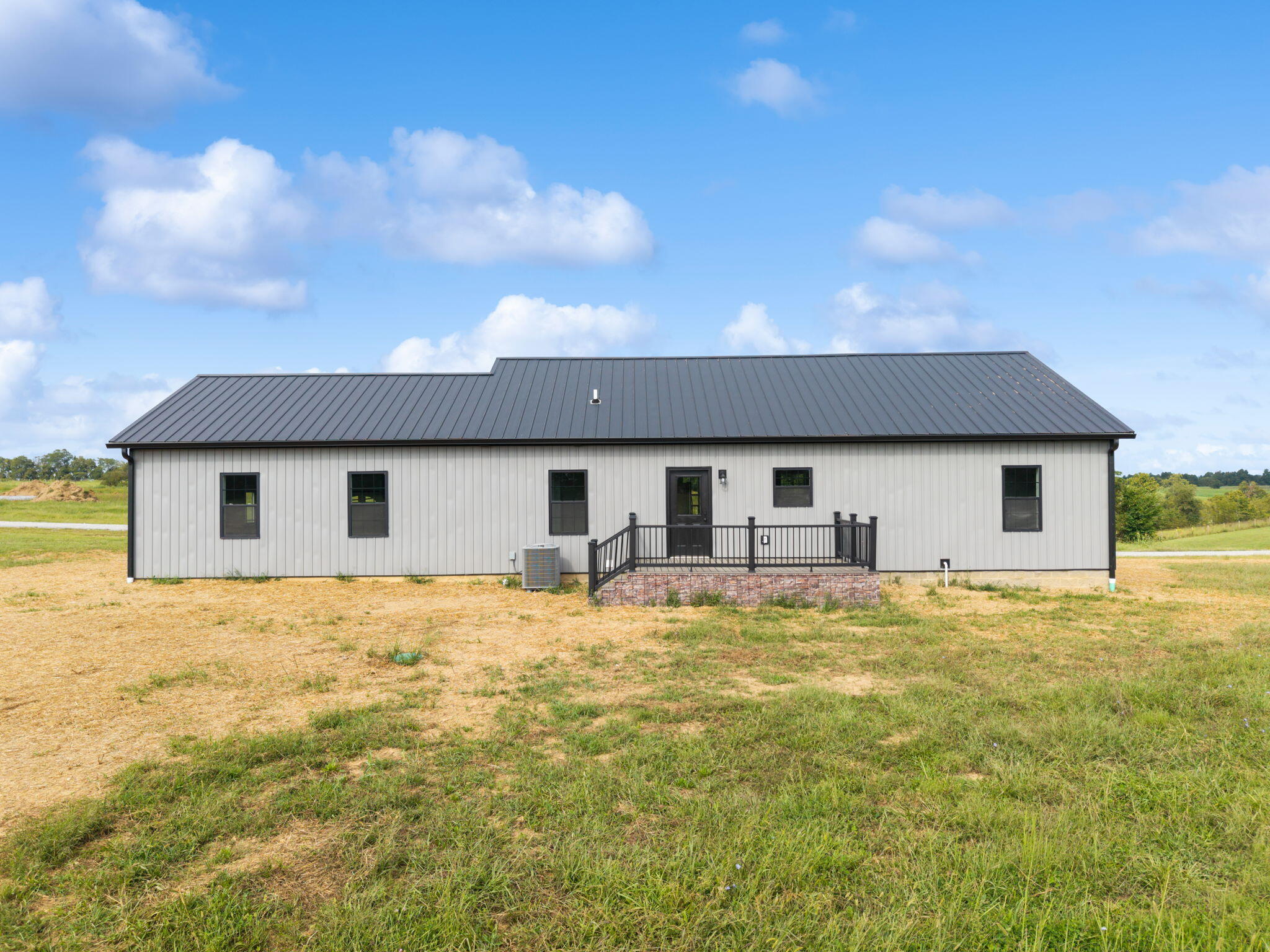 Single-story gray home with a dark metal roof and raised porch in an open grassy yard.