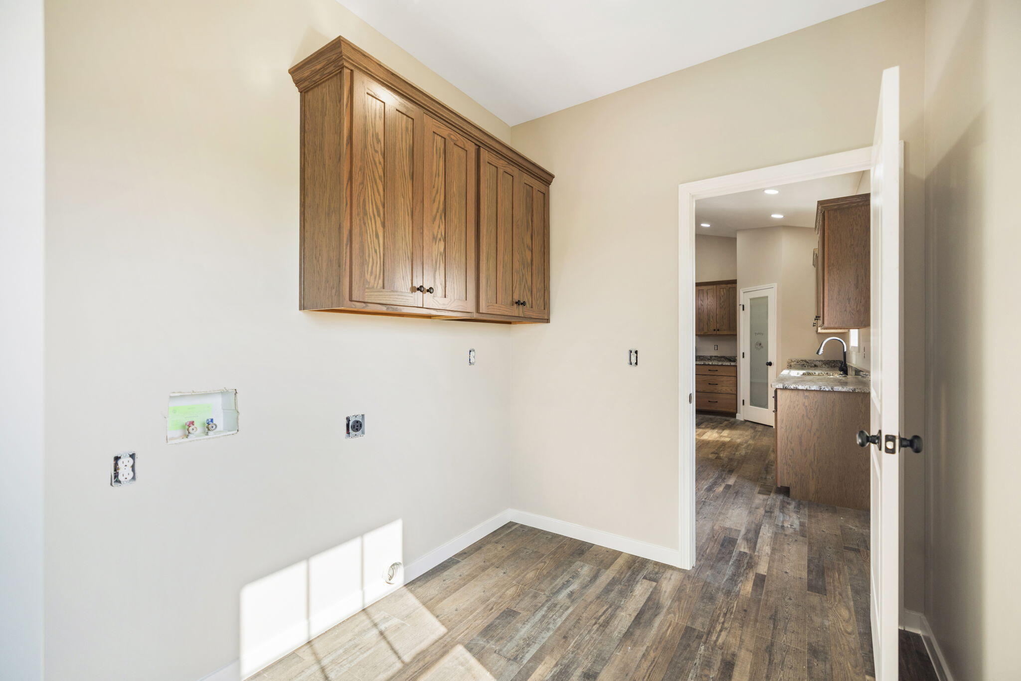 Laundry area with wood cabinets and appliance hookups, opening to a kitchen.