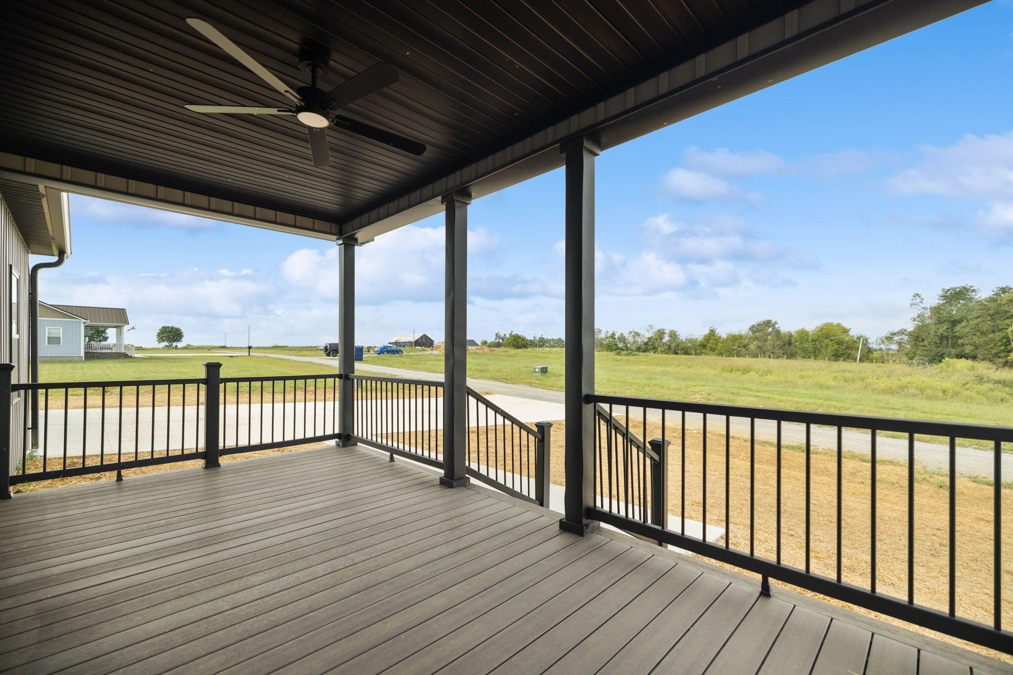 Covered porch with gray decking and black railings overlooking an open grassy lot.