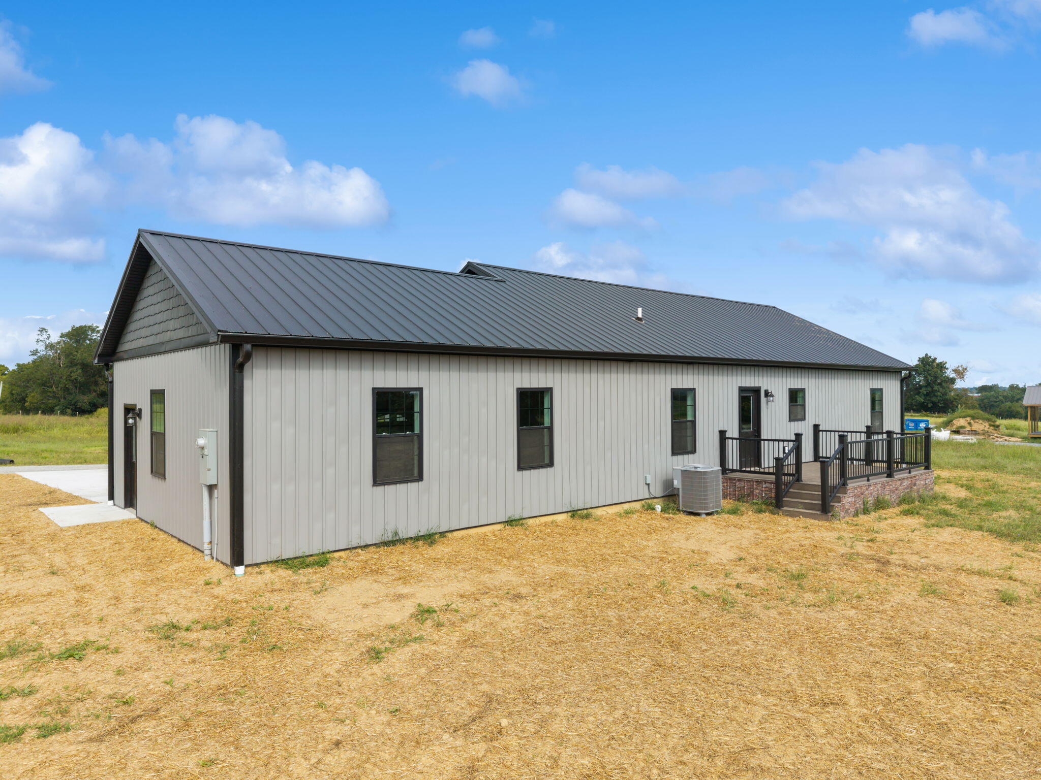 Single-story gray home with a dark metal roof and raised deck on a rural lot.