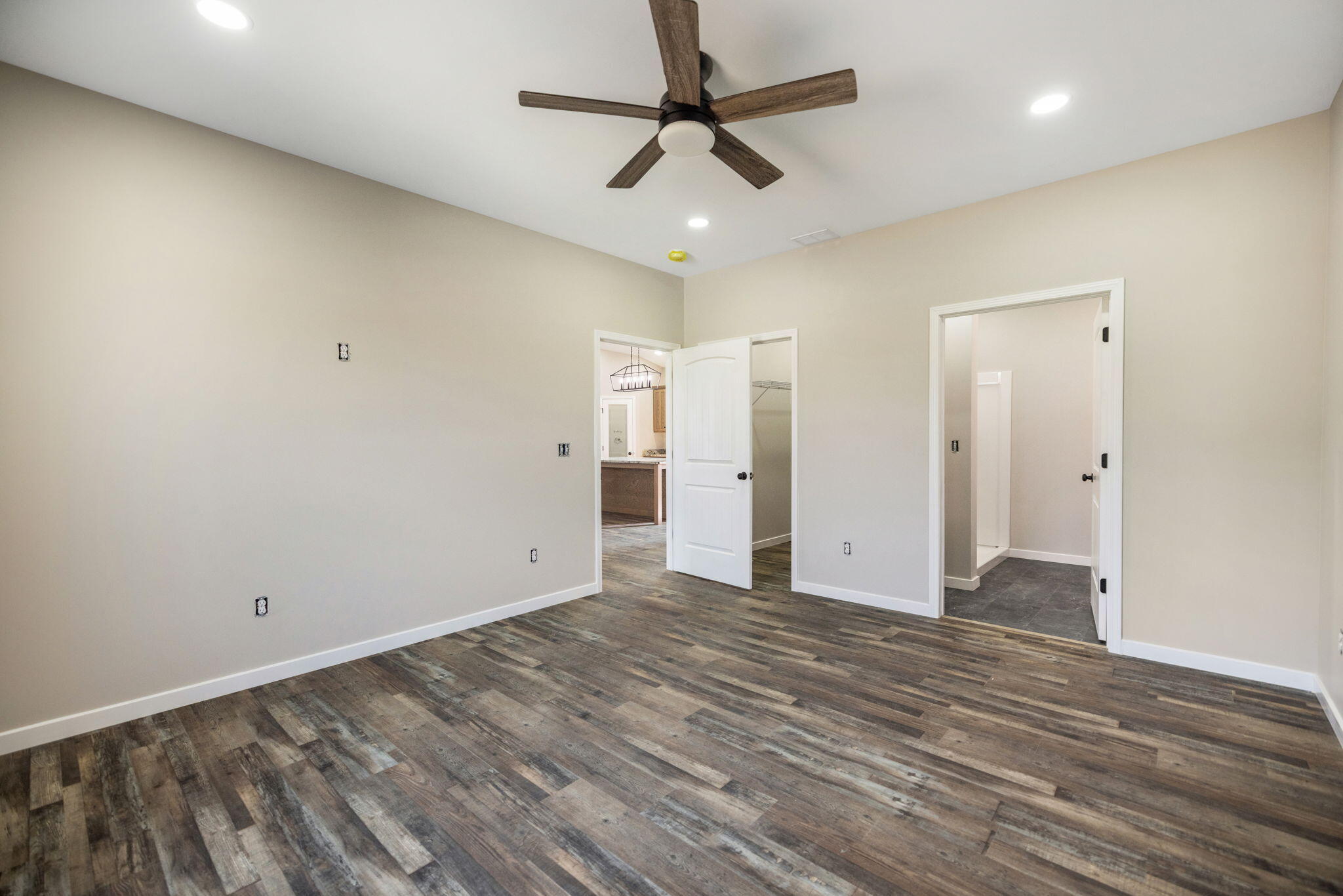Empty bedroom with wood-look floors, ceiling fan, and open doors to a closet and bathroom.