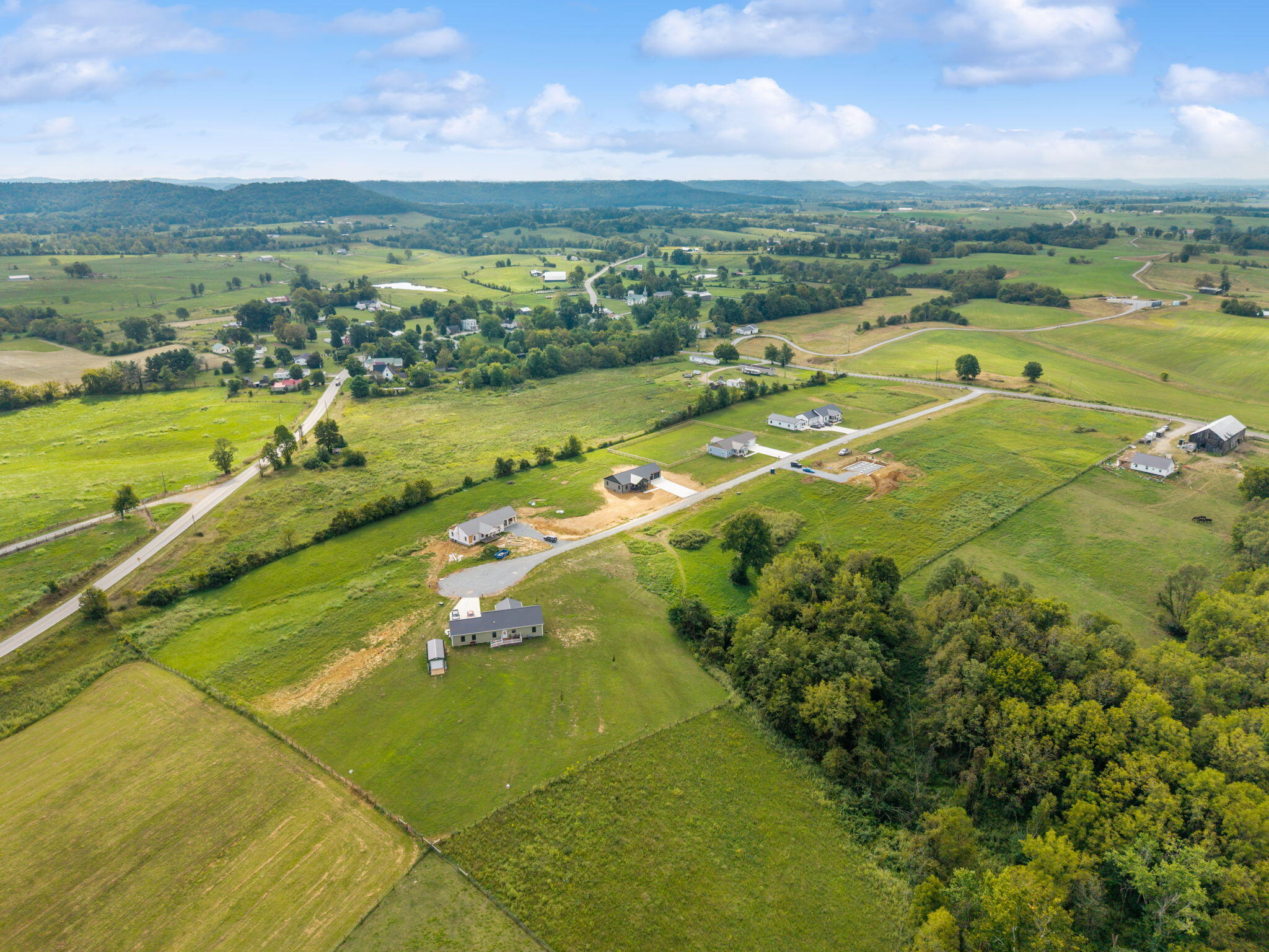 Aerial view of rural homes and fields, with country roads and wooded hills in the distance.