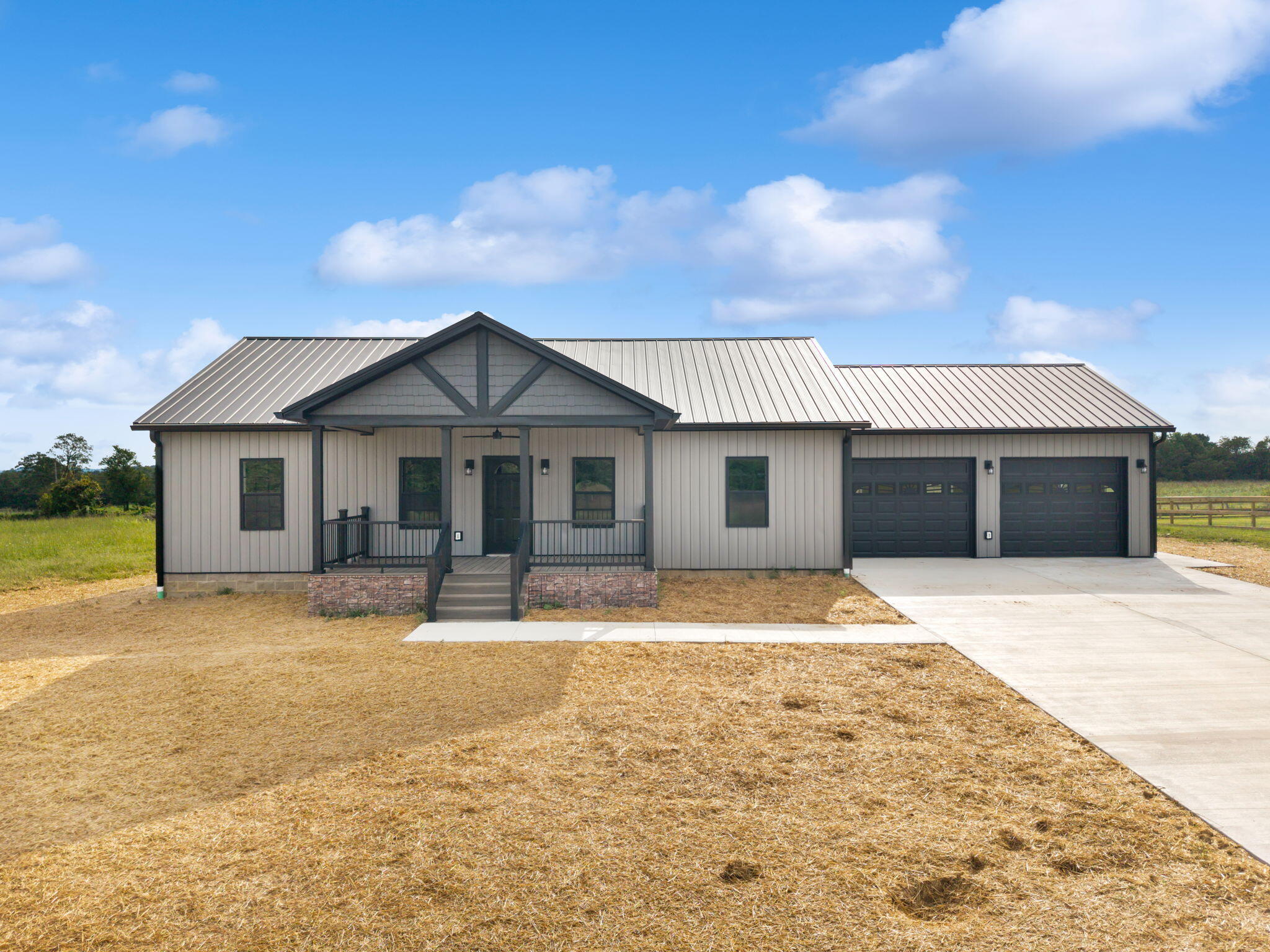 Single-story home with a covered porch, gray metal roof, and two-car garage.