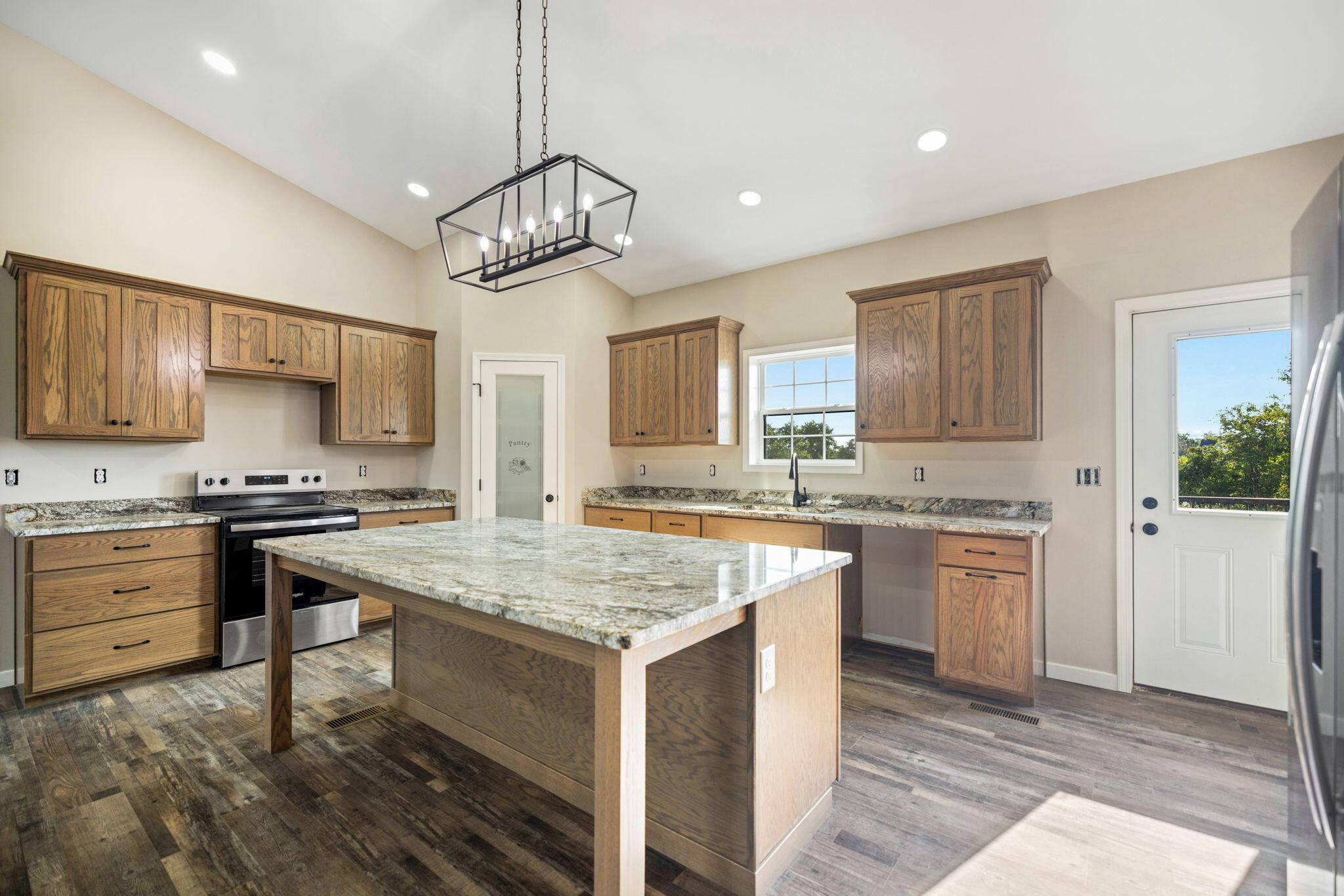 Kitchen with a large granite island, natural wood cabinets, and stainless steel range.