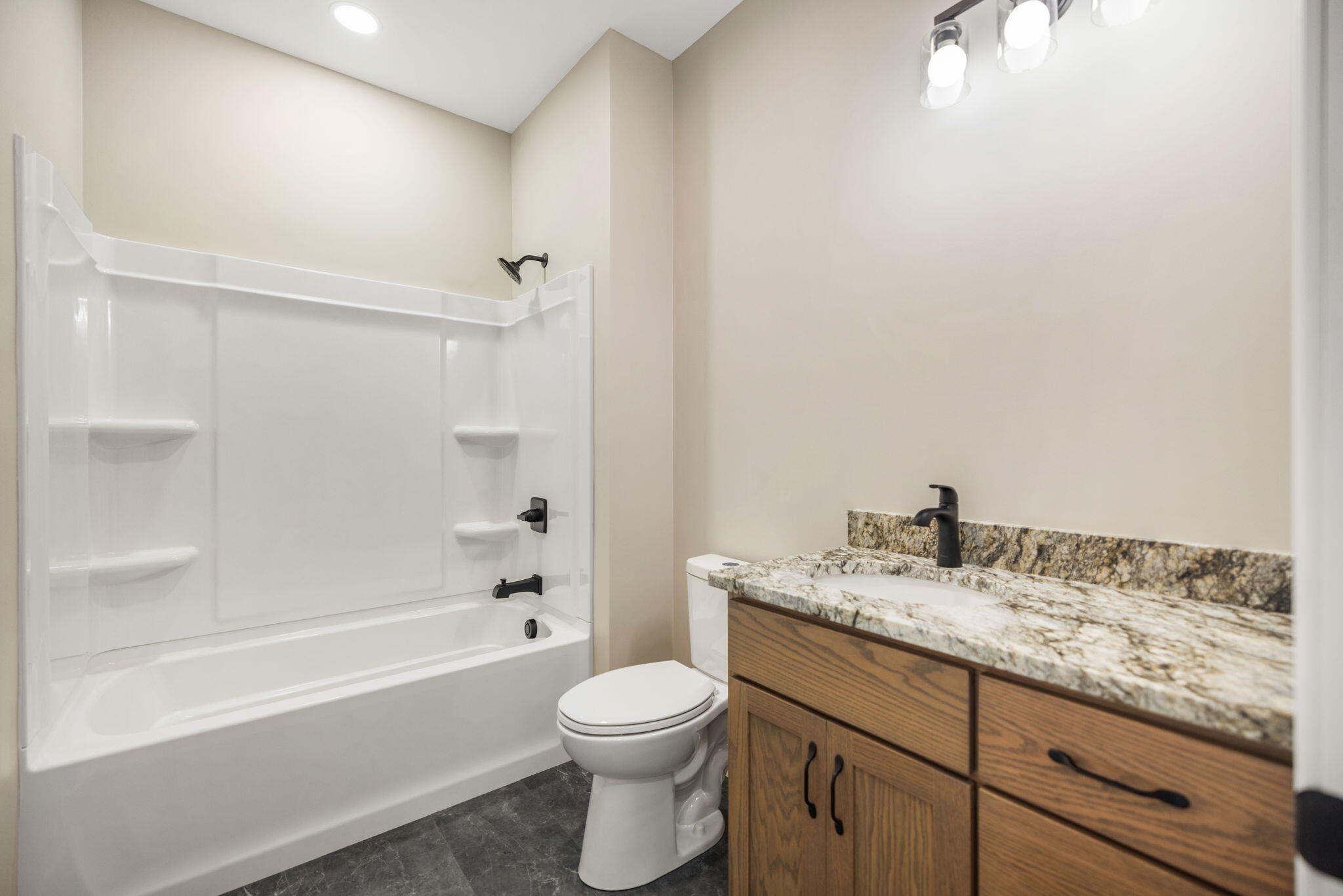 Bathroom with a white tub and shower beside a wood vanity with a marbled countertop.