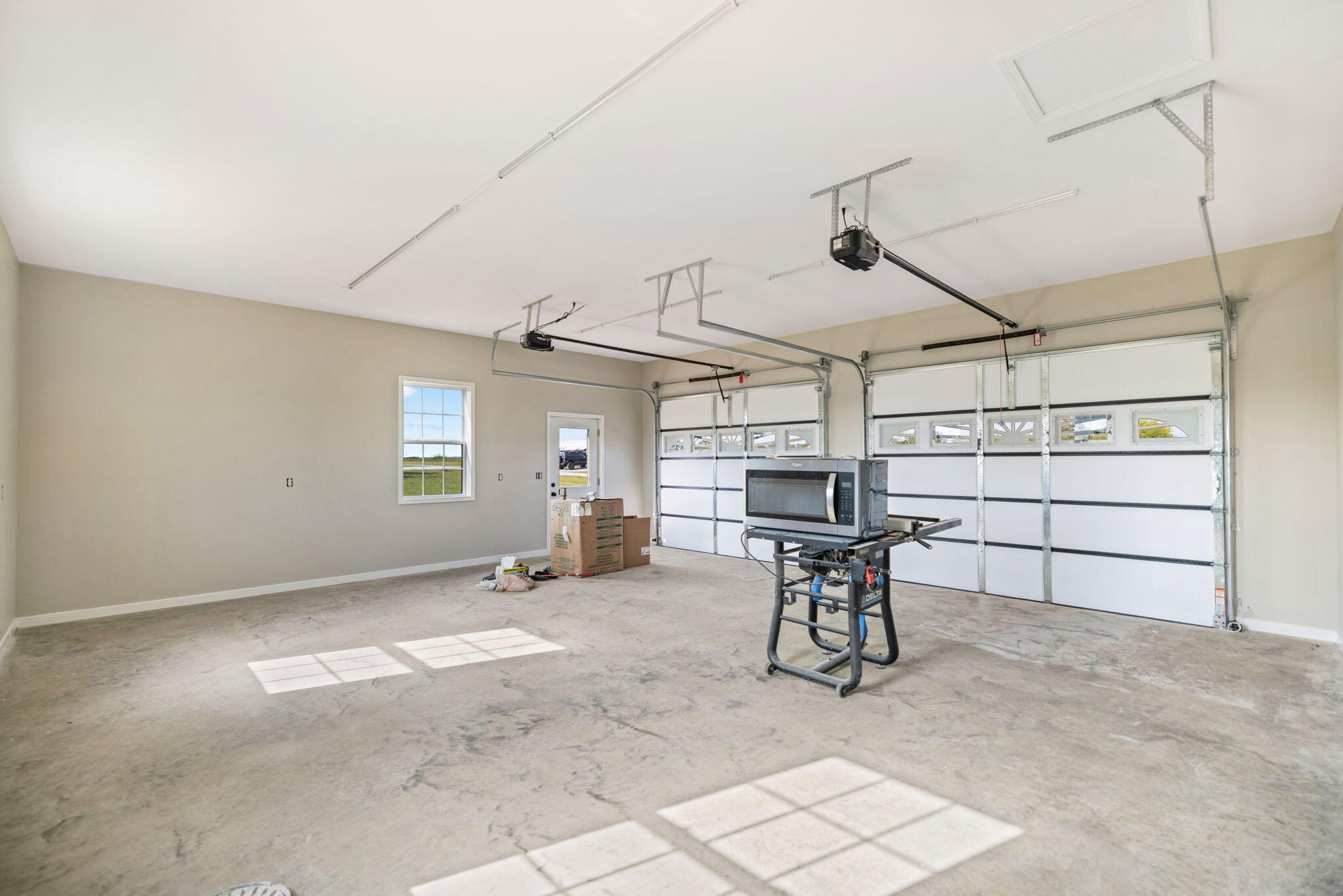Spacious two-car garage with two windowed doors and a workbench saw on the concrete floor.