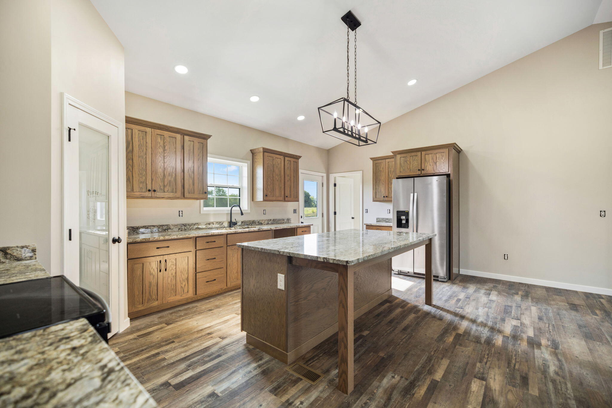 Kitchen with a large granite-topped island, natural wood cabinets, and stainless steel refrigerator.