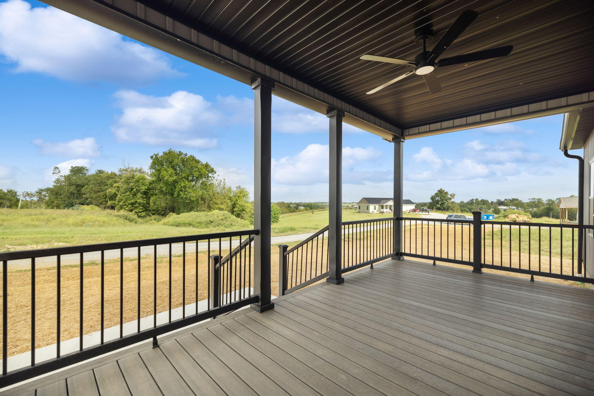 Covered porch with gray decking and black railings overlooking open fields.