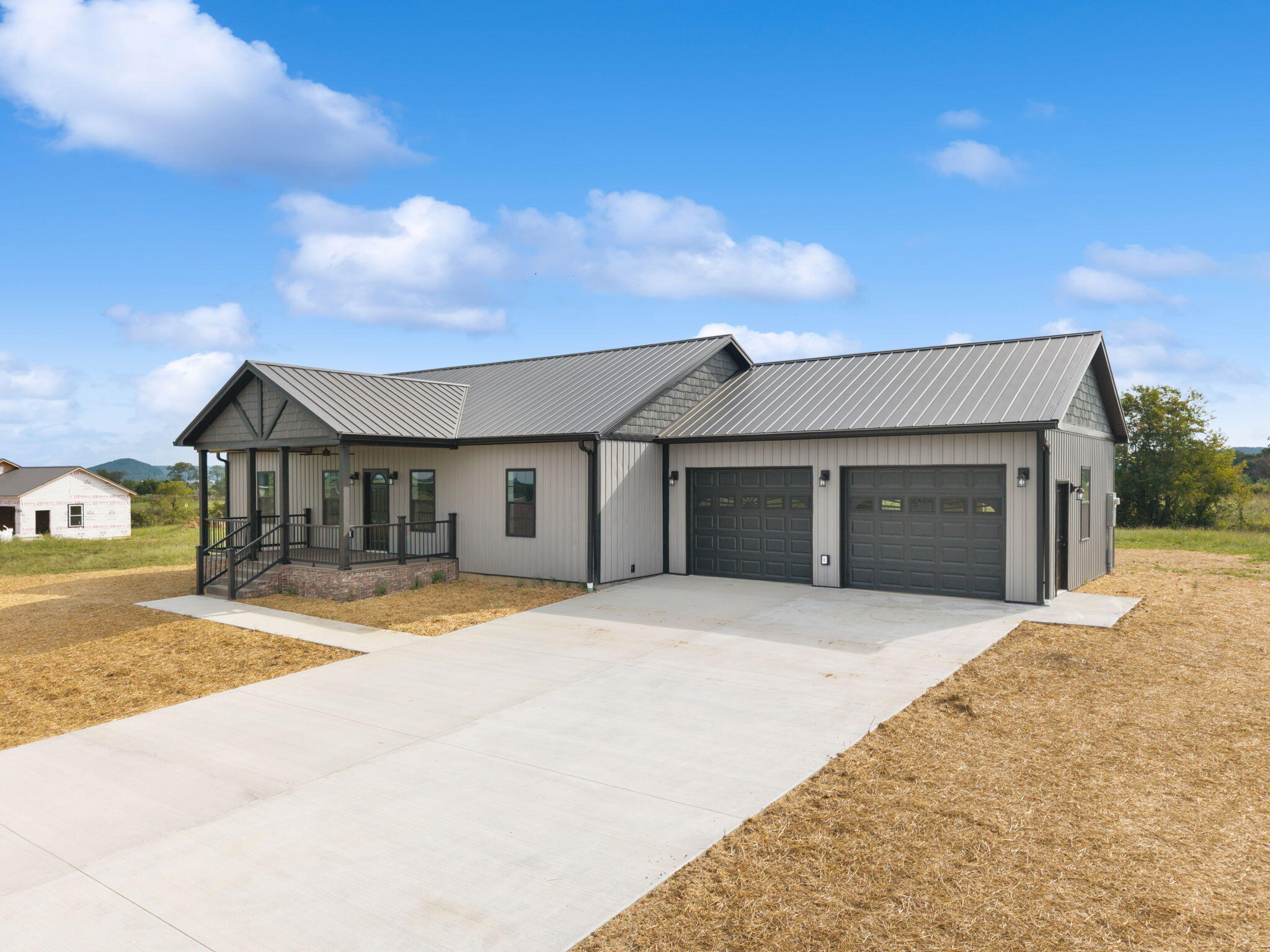 Gray single-story home with a metal roof, covered porch, two-car garage, and broad concrete driveway.