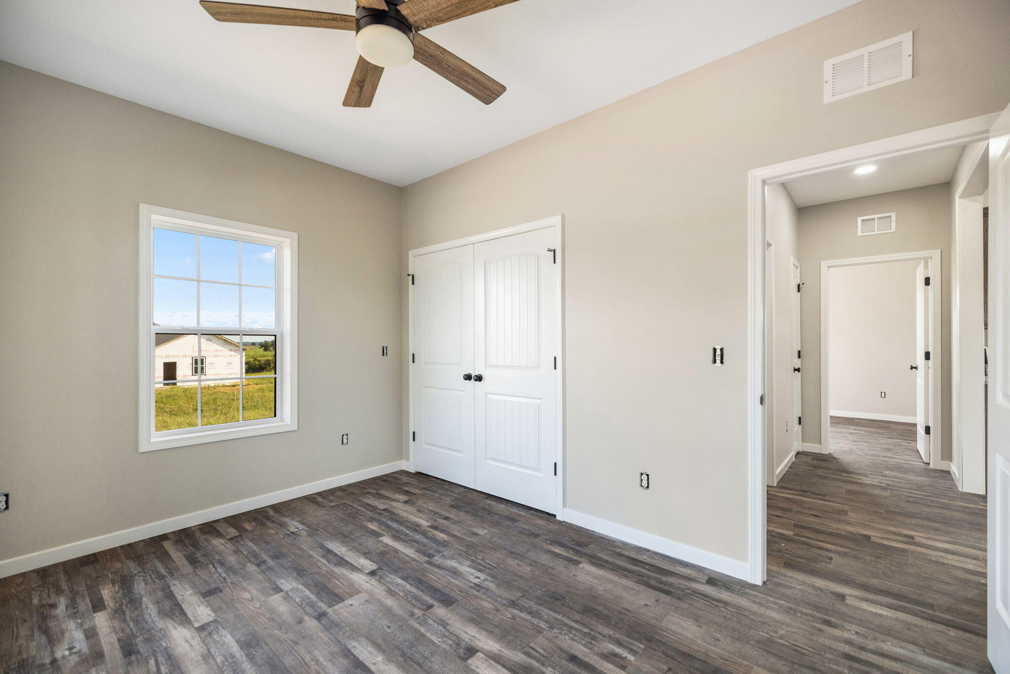 Empty bedroom with dark wood-look floors, white double closet doors, and a ceiling fan.