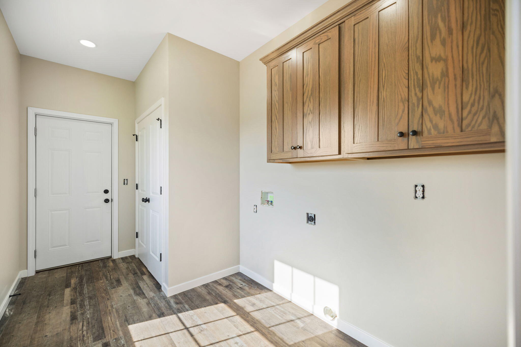 Empty room with natural wood upper cabinets, plank flooring, and a white exterior door.