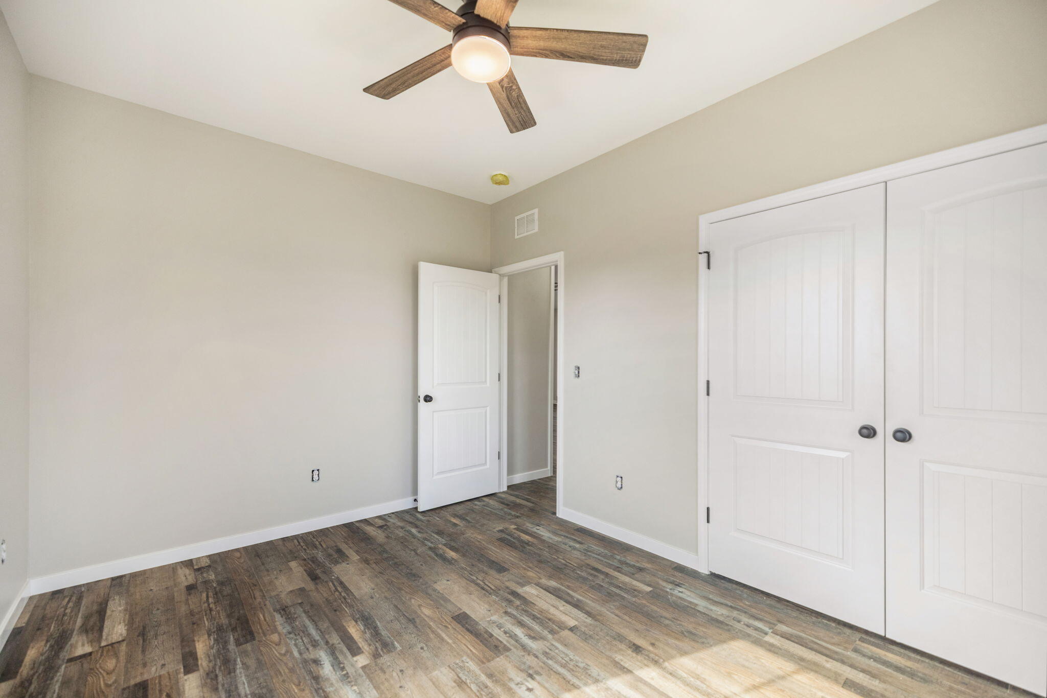 Empty bedroom with a wood-blade ceiling fan, white closet doors, and dark plank flooring.