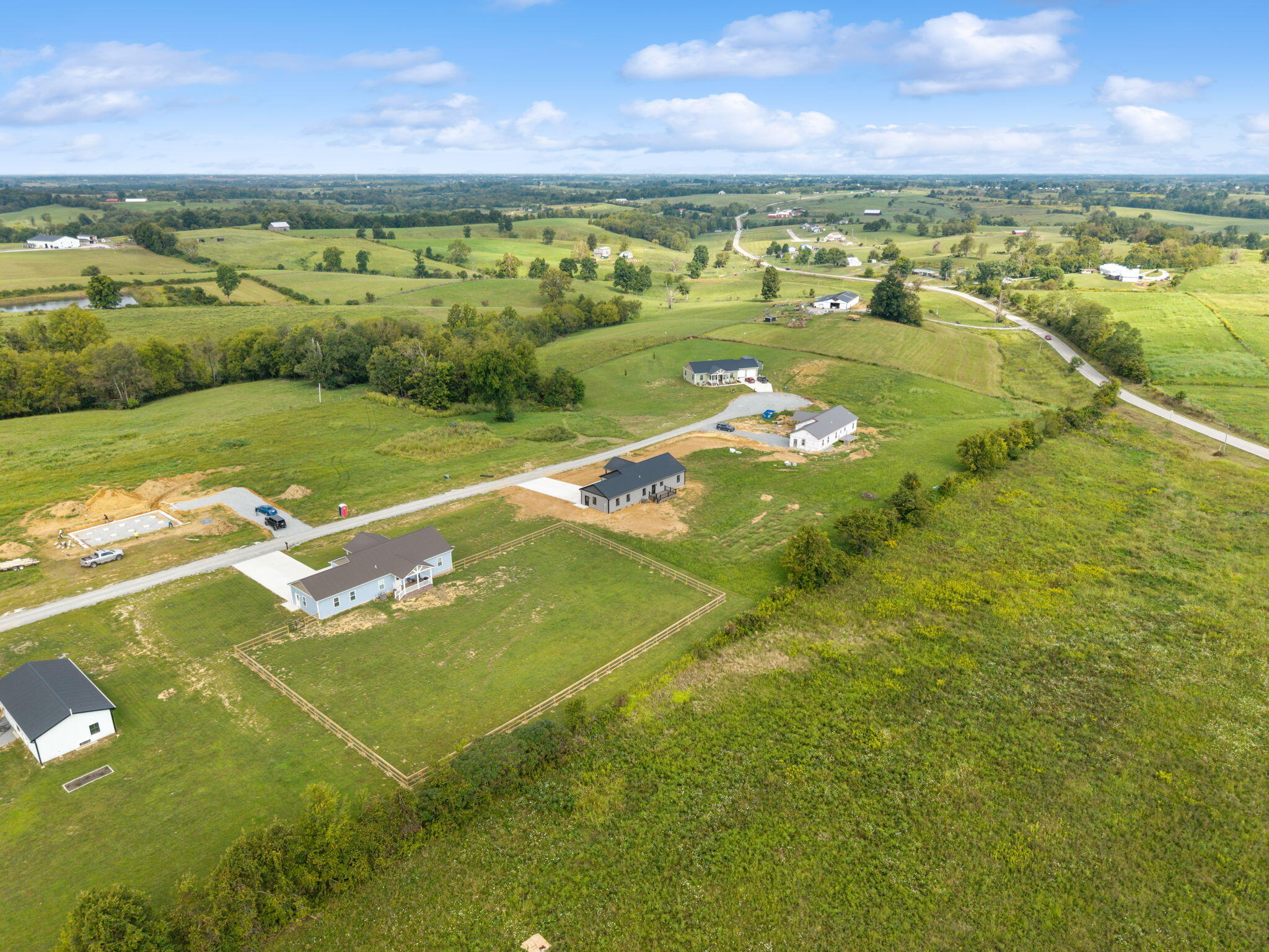 Aerial view of rural homes among green fields, with a fenced yard and winding country roads.