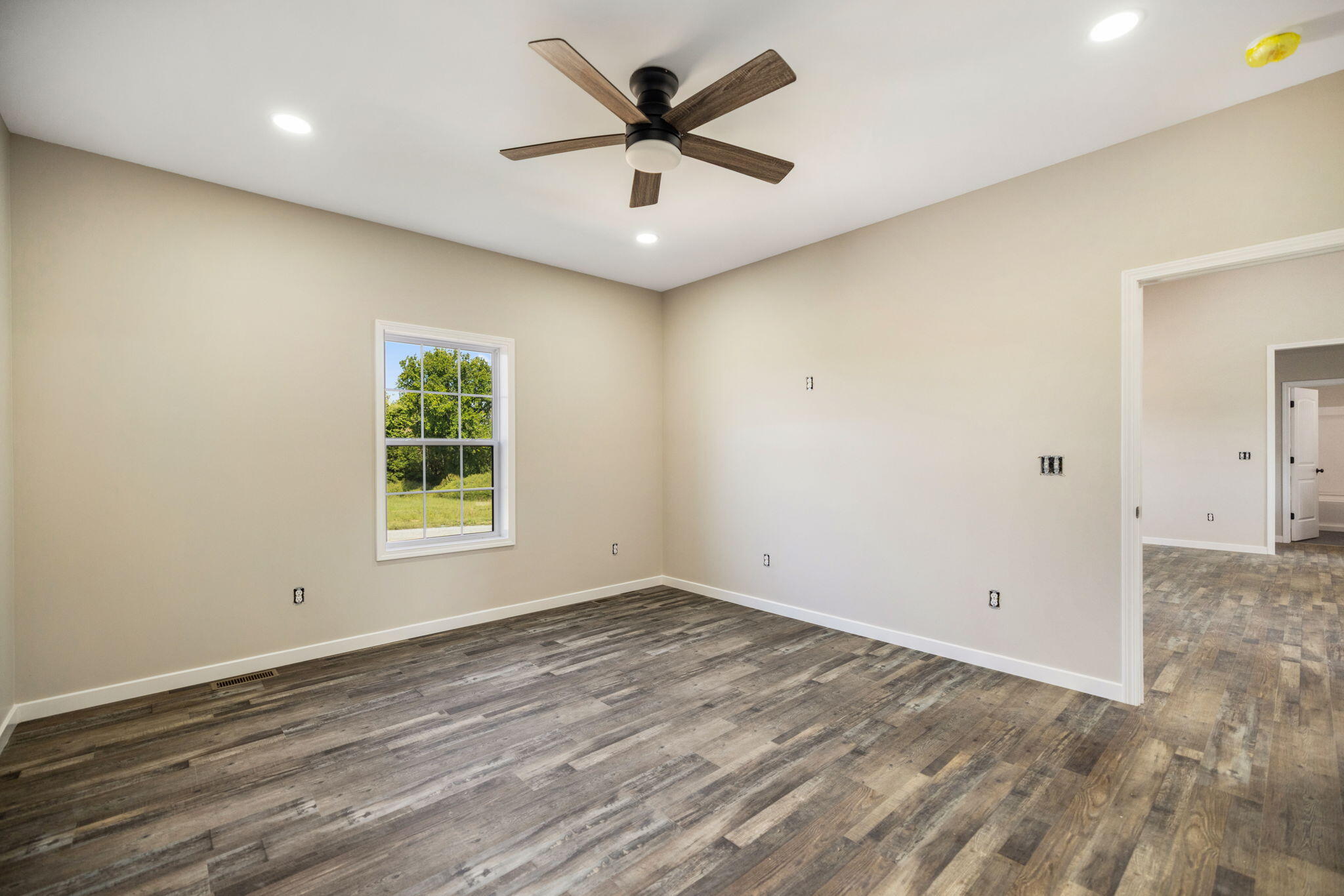 Unfurnished room with plank flooring, a ceiling fan, and a window overlooking trees and lawn.