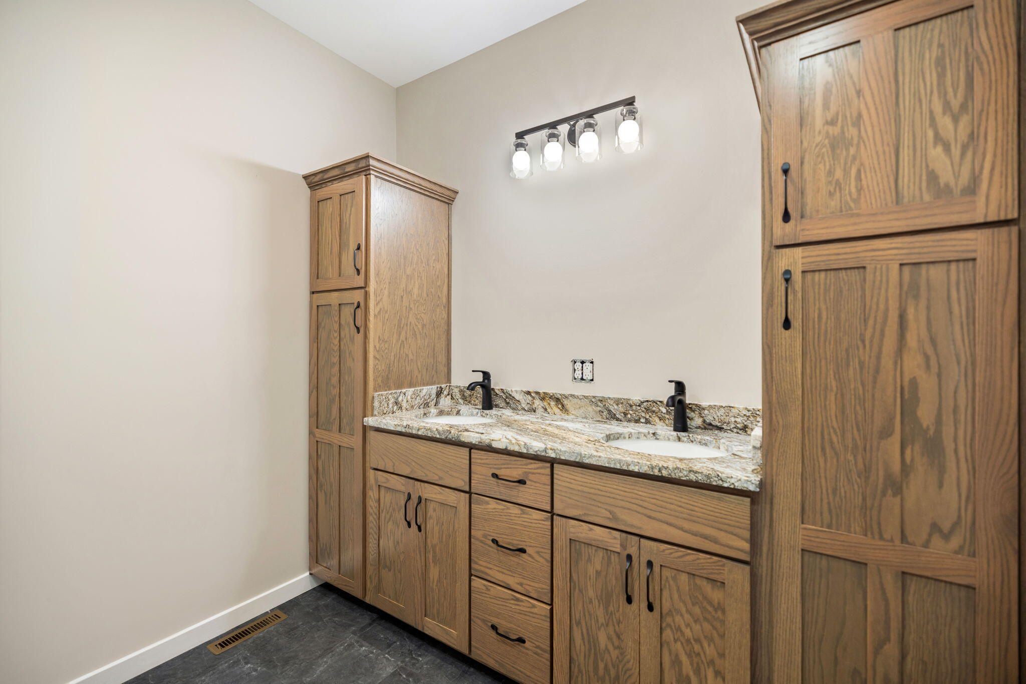 Bathroom vanity with double sinks, oak cabinetry, marbled countertops, and black faucets.