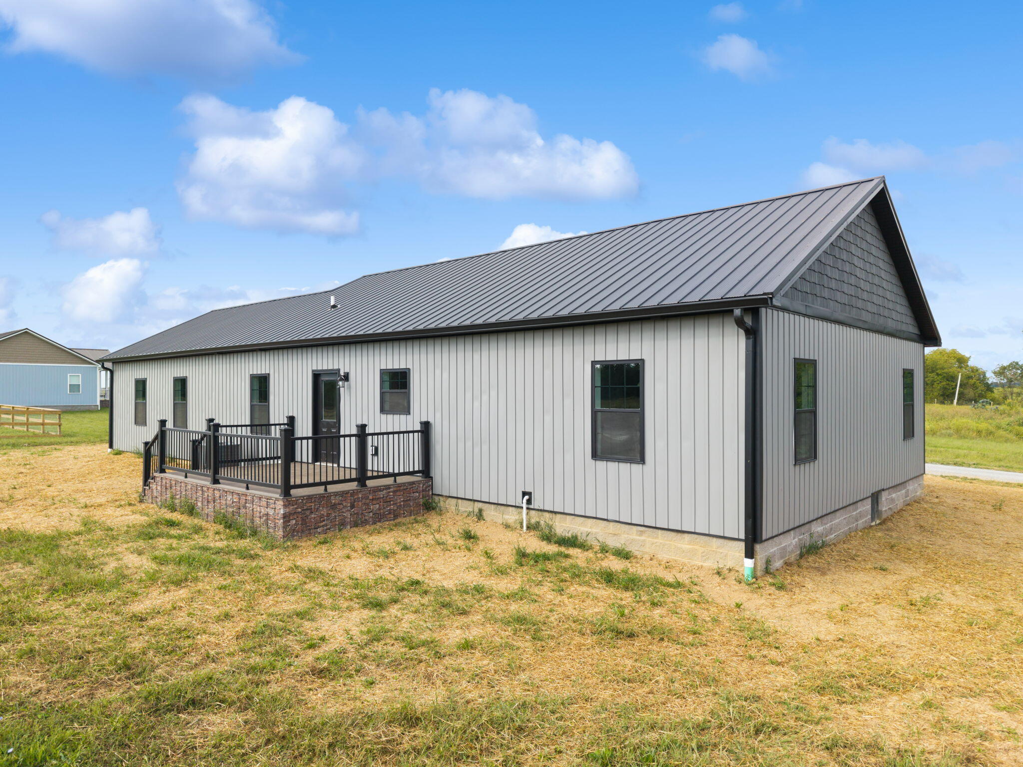 Gray-sided home with a dark metal roof and raised deck in a grassy yard.