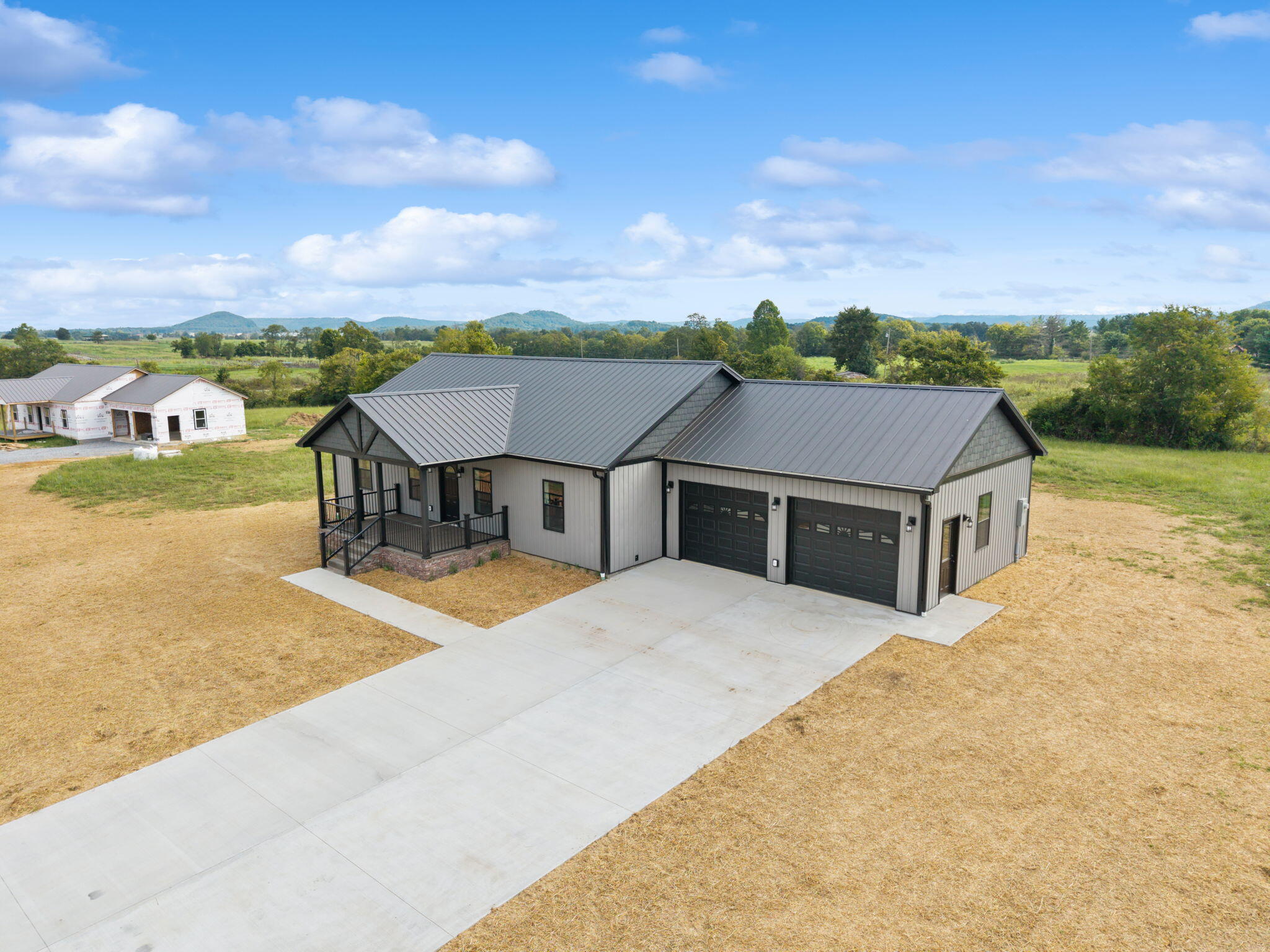 Gray single-story home with a metal roof, covered porch, two garage doors, and a broad concrete driveway.