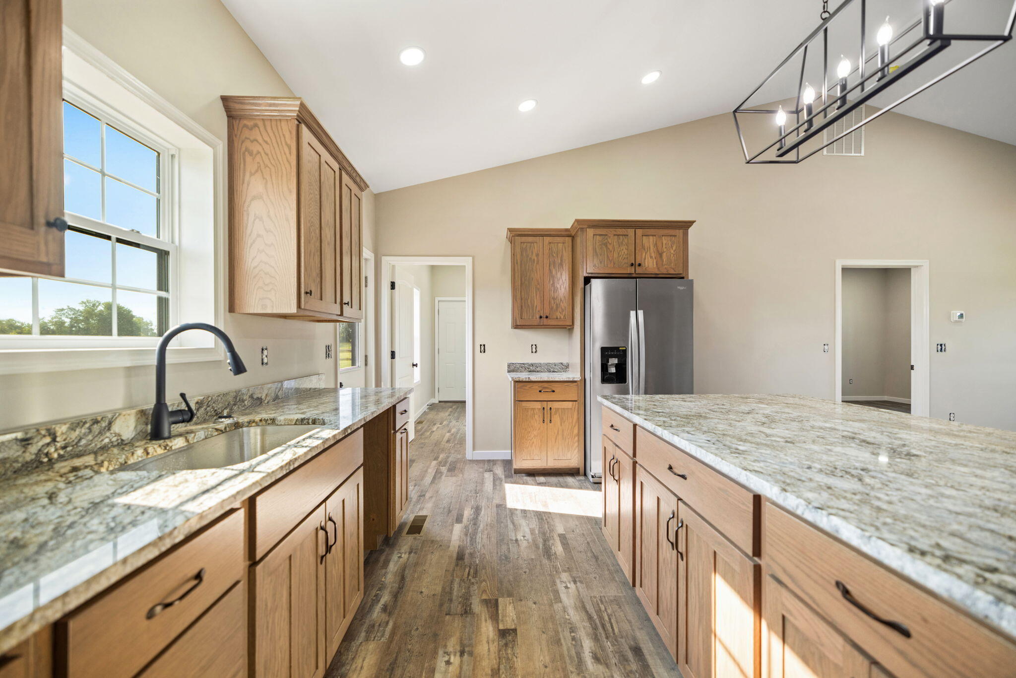 Kitchen with wood cabinetry, granite counters, a large island, and stainless steel refrigerator.