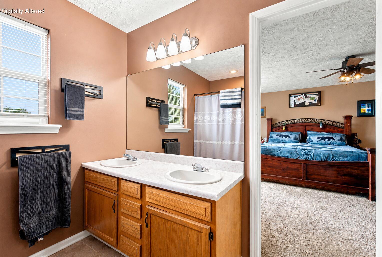 Bathroom with a double-sink wood vanity and large mirror opening onto a bedroom.