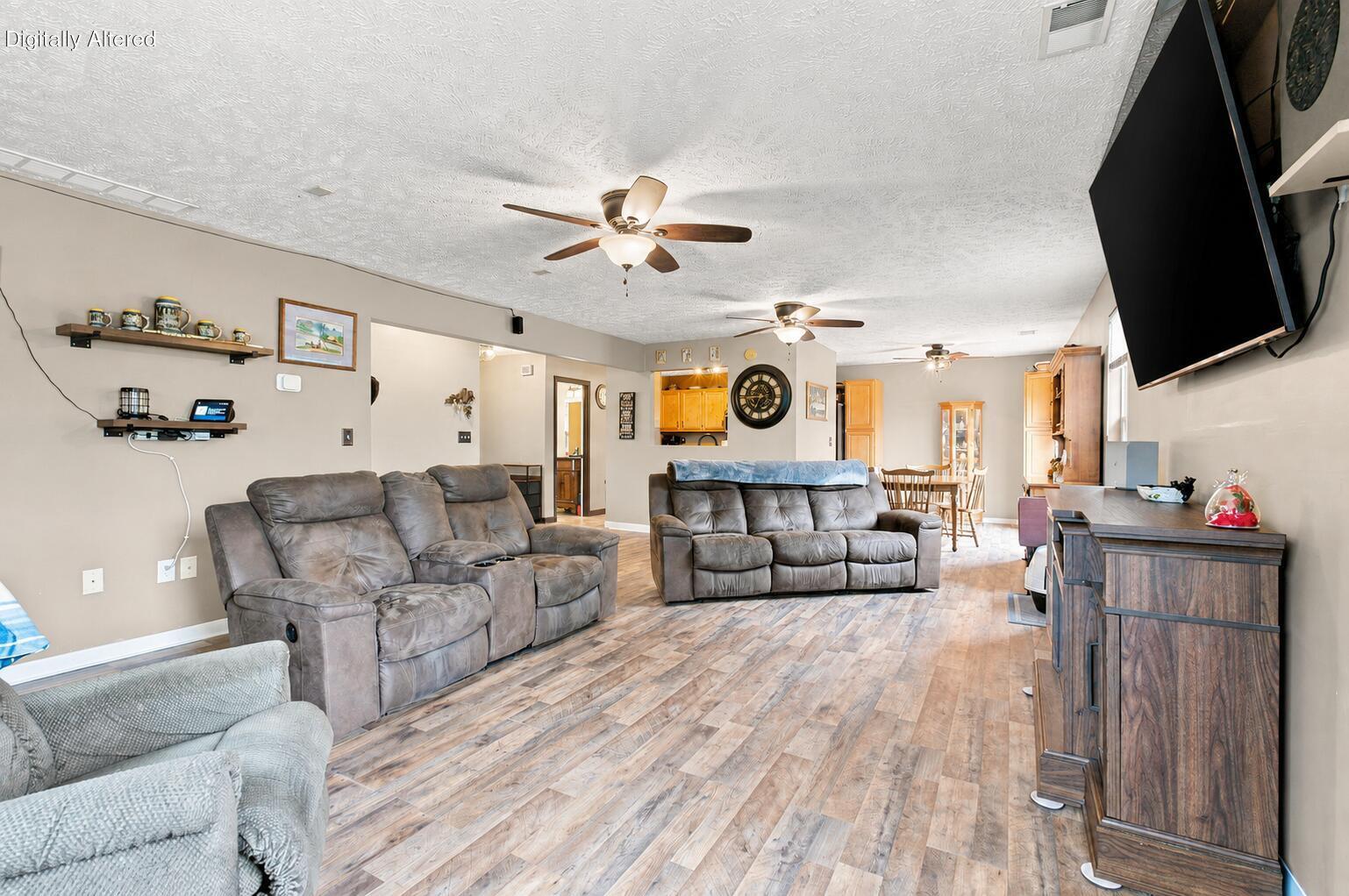 Furnished living room with gray reclining sofas, wood-look flooring, and an open dining area.