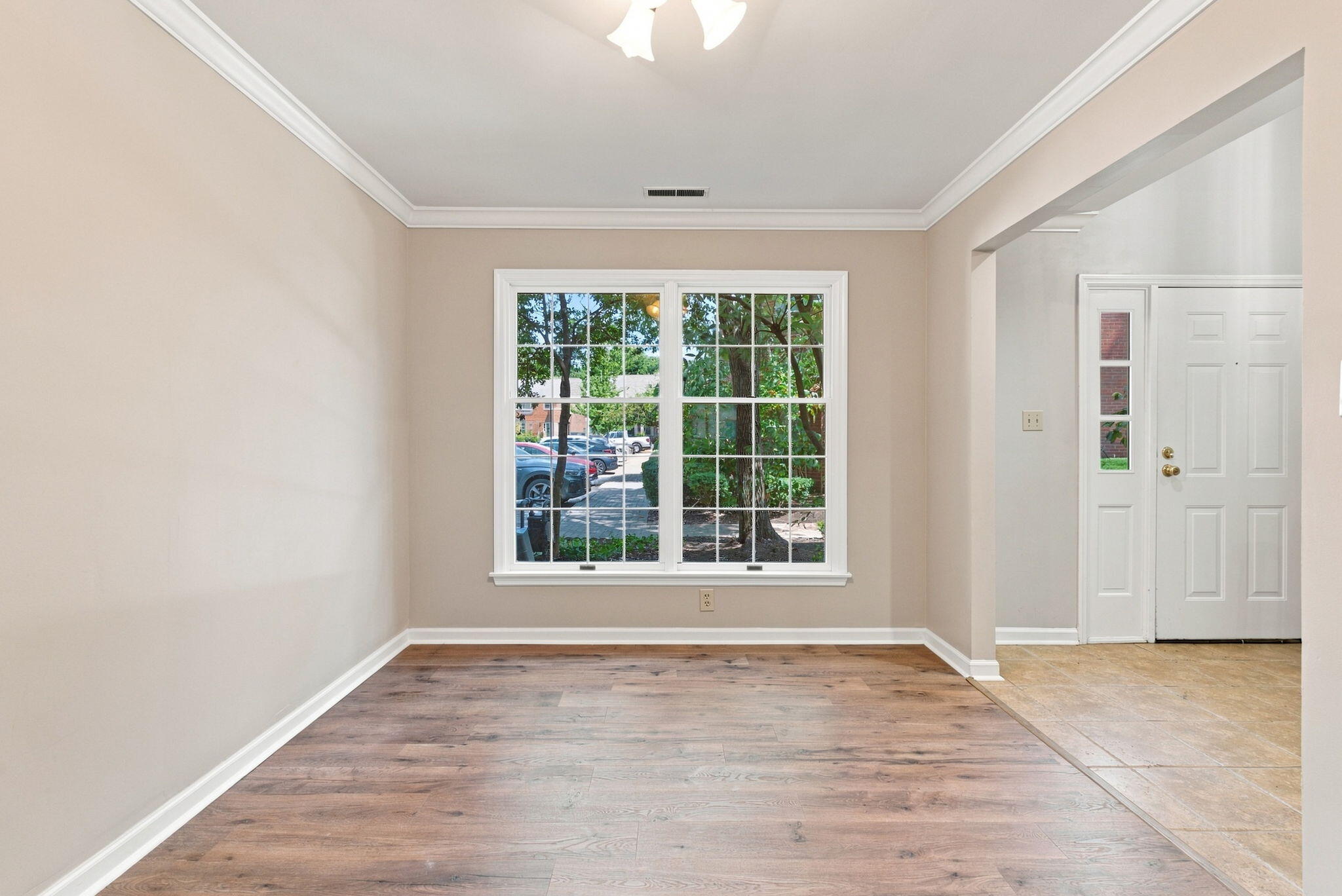 Vacant room with wood-look floors, a large divided-pane window, and a tiled entryway.