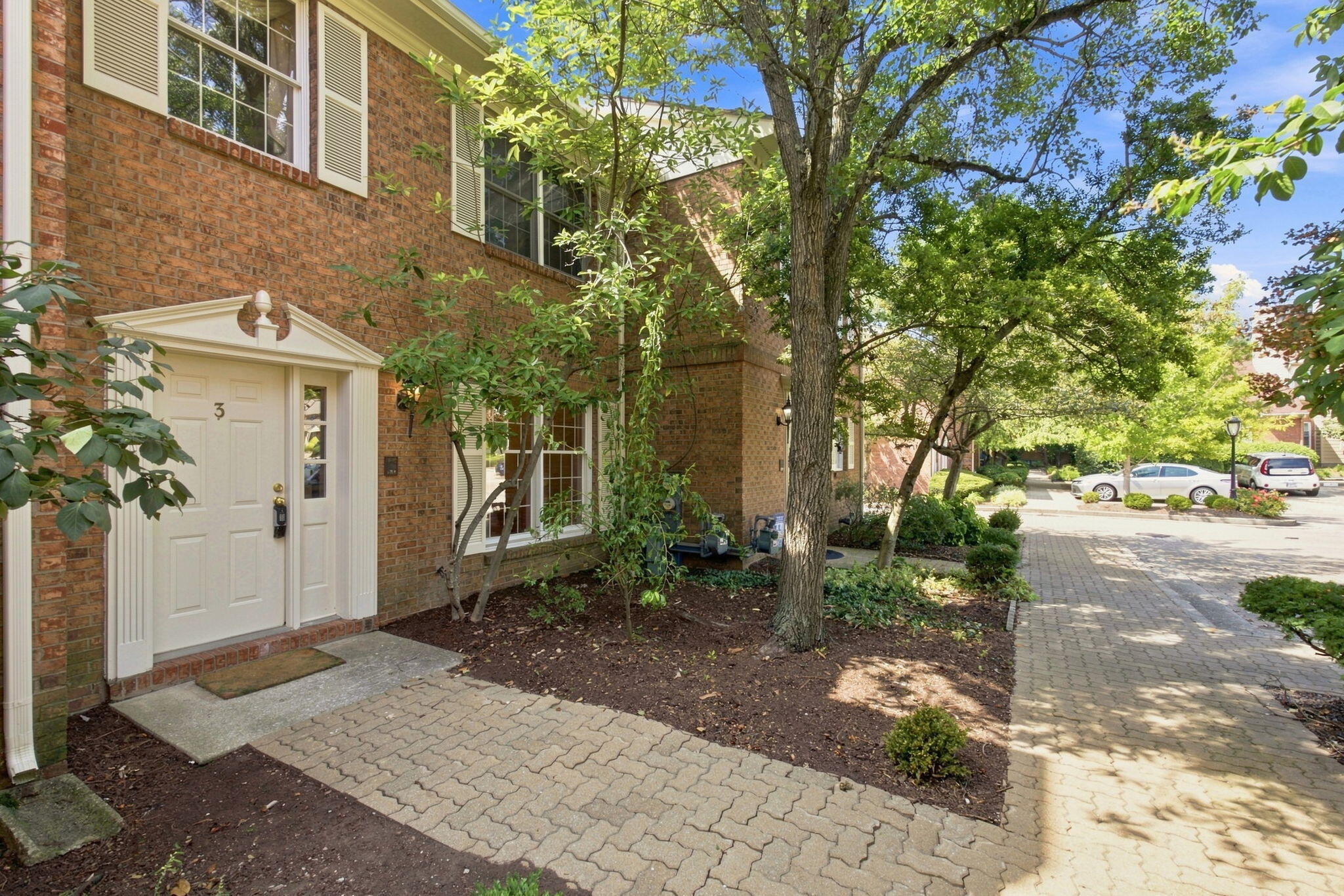 Brick residence entrance marked 3 beside a landscaped walkway shaded by mature trees.