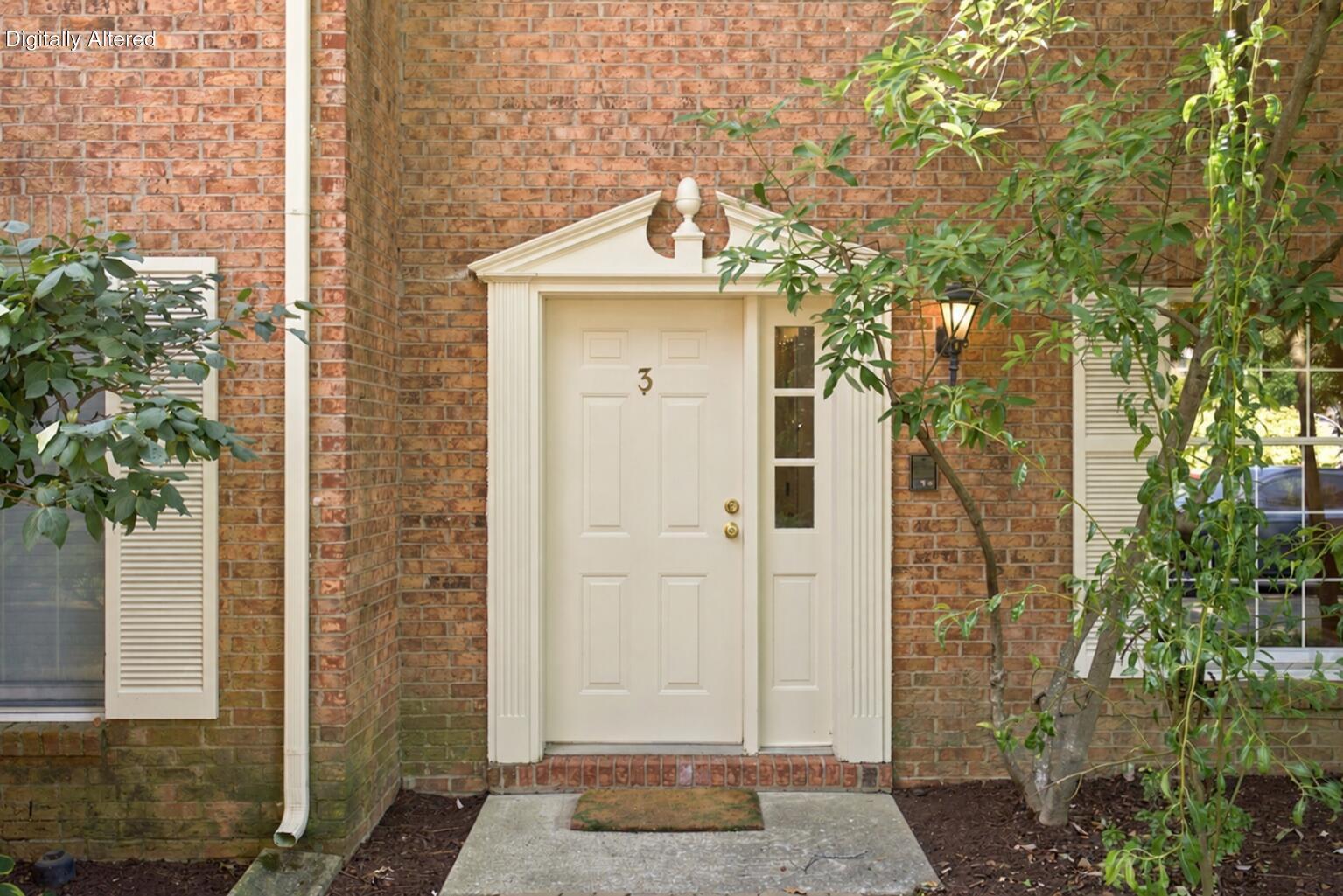 Brick townhouse entrance with white-trimmed door numbered 3, framed by leafy trees.