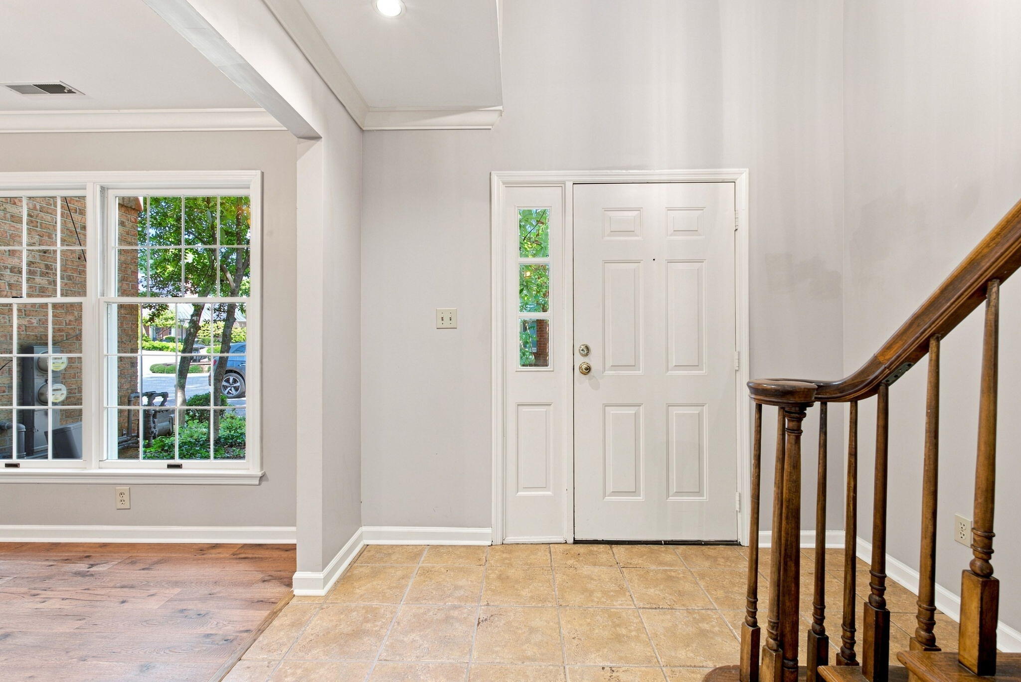Entryway with a white front door, large window, tiled floor, and wooden staircase railing.