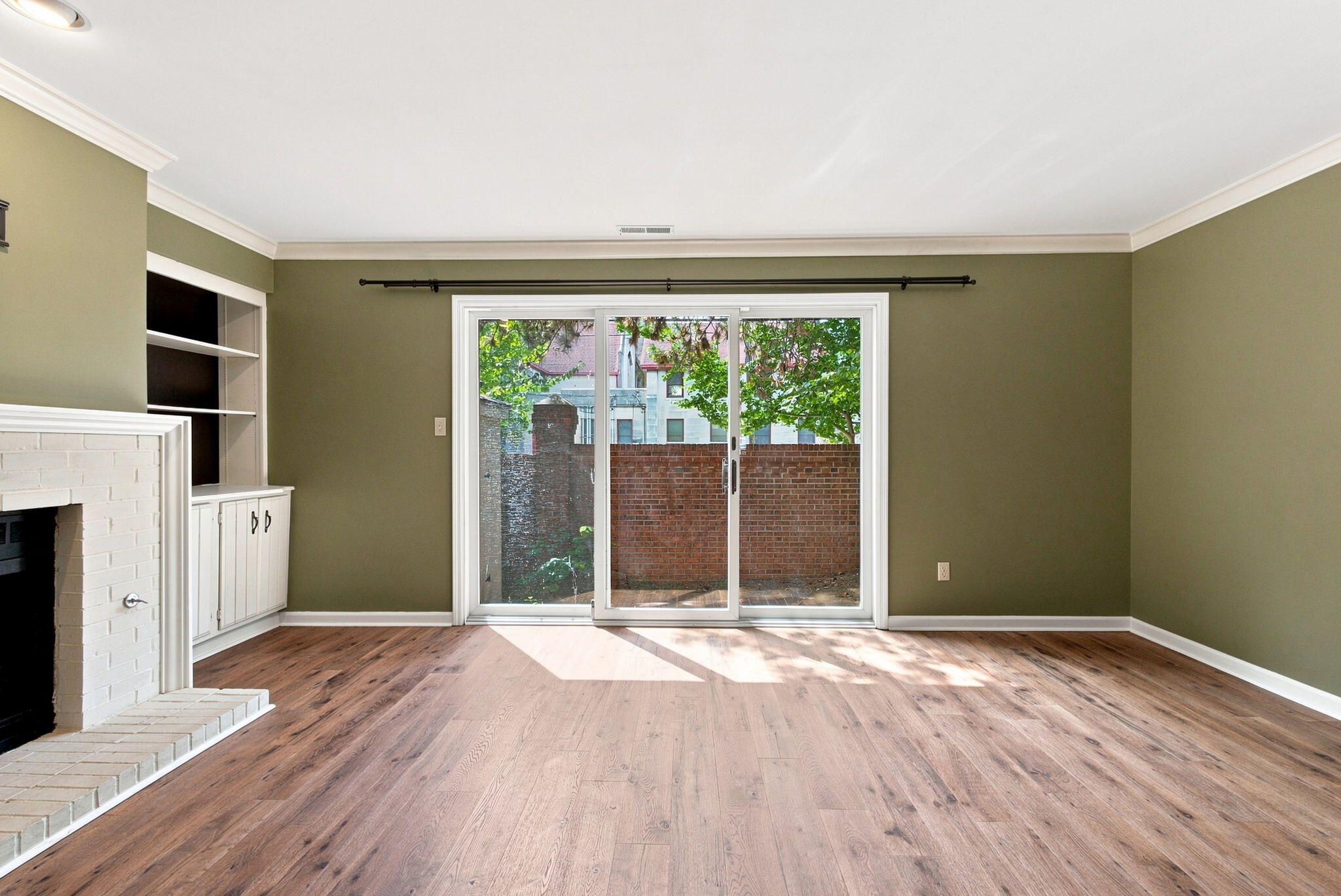 Living room with wood floors, a white brick fireplace, built-in shelves, and sliding glass doors.