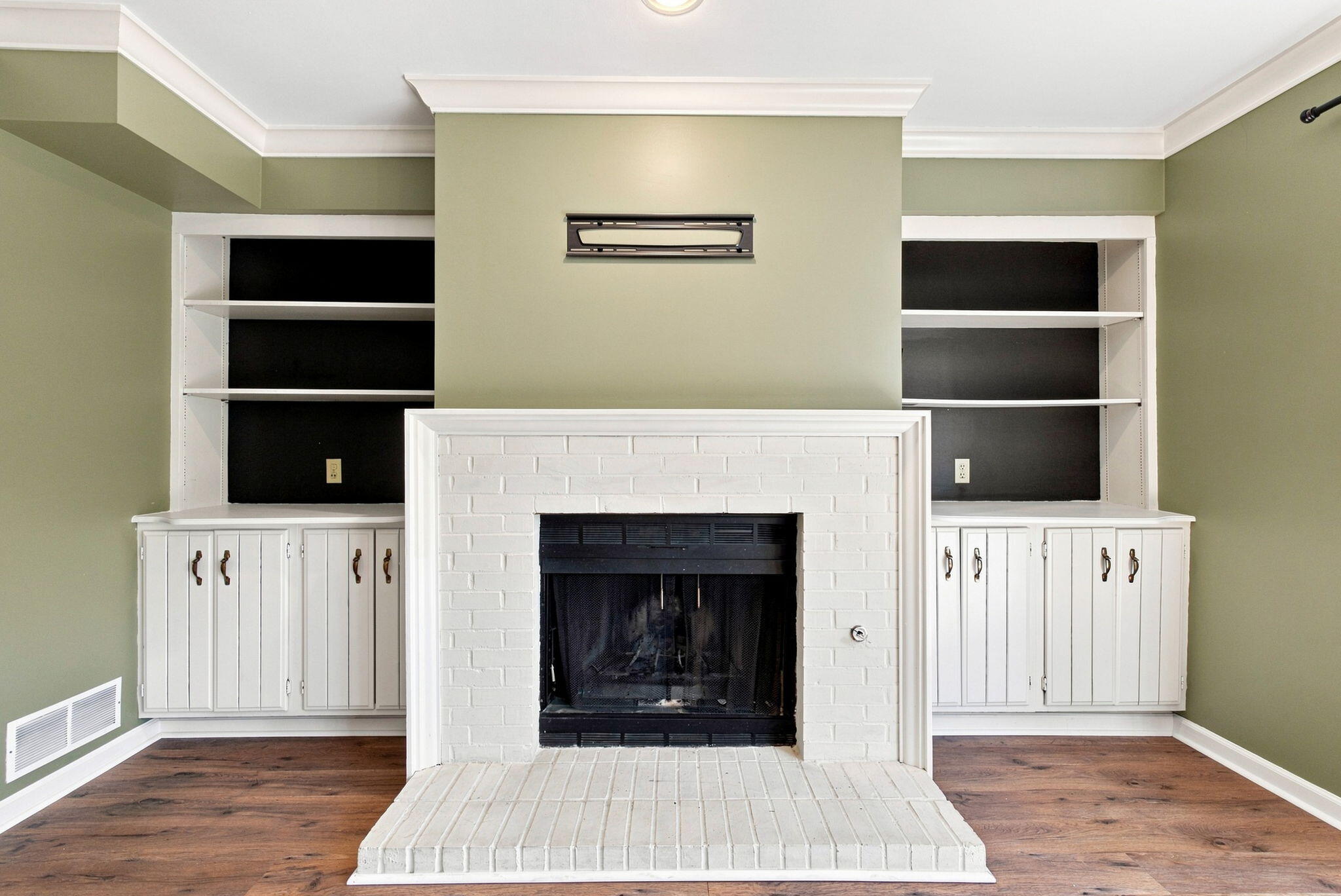White brick fireplace flanked by built-in cabinets and shelving in a room with wood floors.
