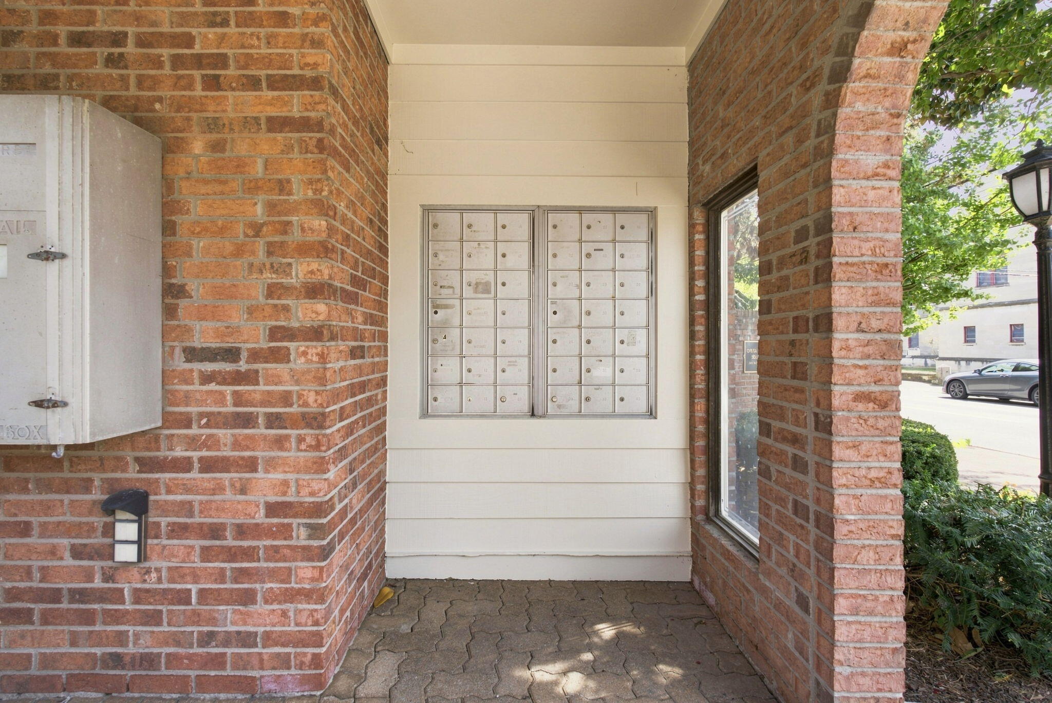 Covered brick building entrance with wall-mounted mailboxes and a paved walkway.