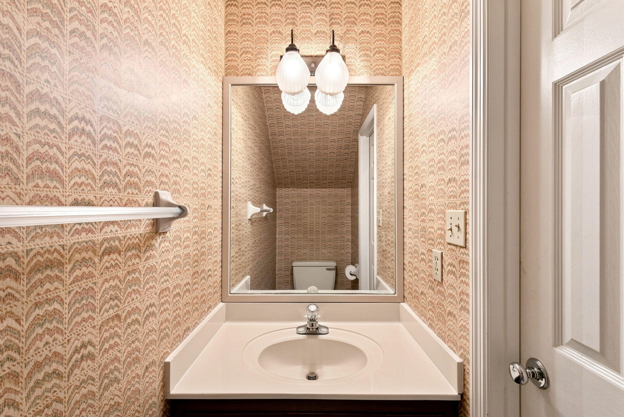 Bathroom vanity with patterned wallpaper, a large mirror, and a towel bar.