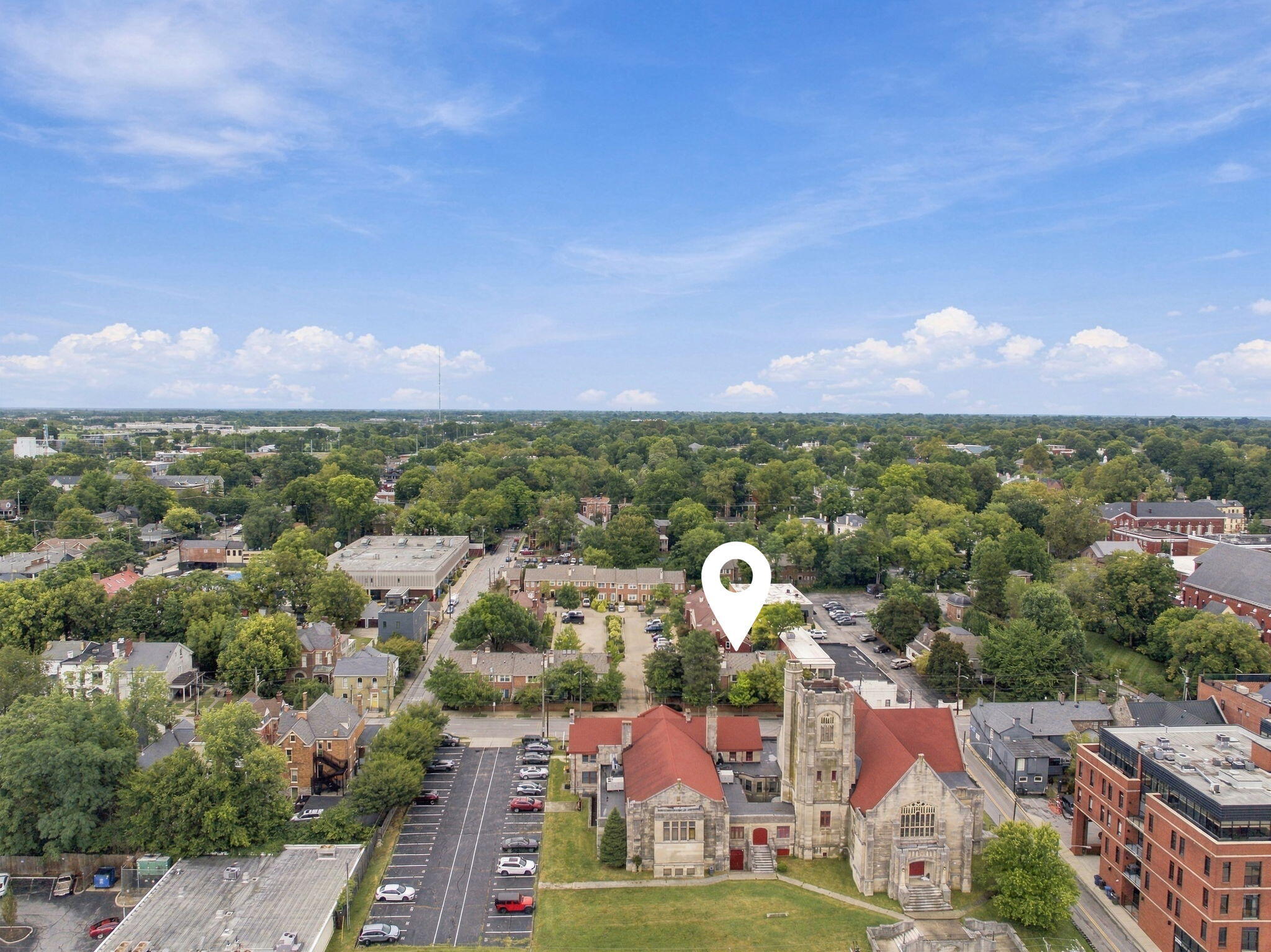 Aerial neighborhood view with a map pin marking the property beside a stone church.