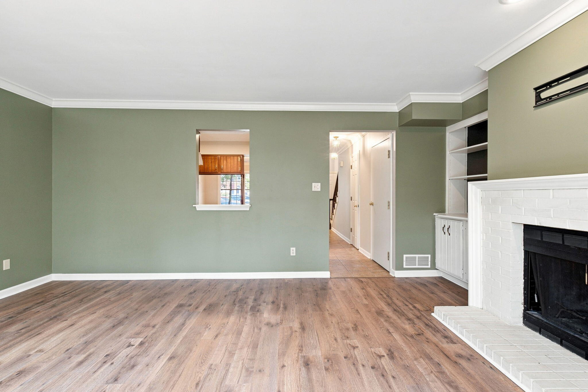 Unfurnished living room with wood-look floors, green walls, built-in shelving, and a white brick fireplace.