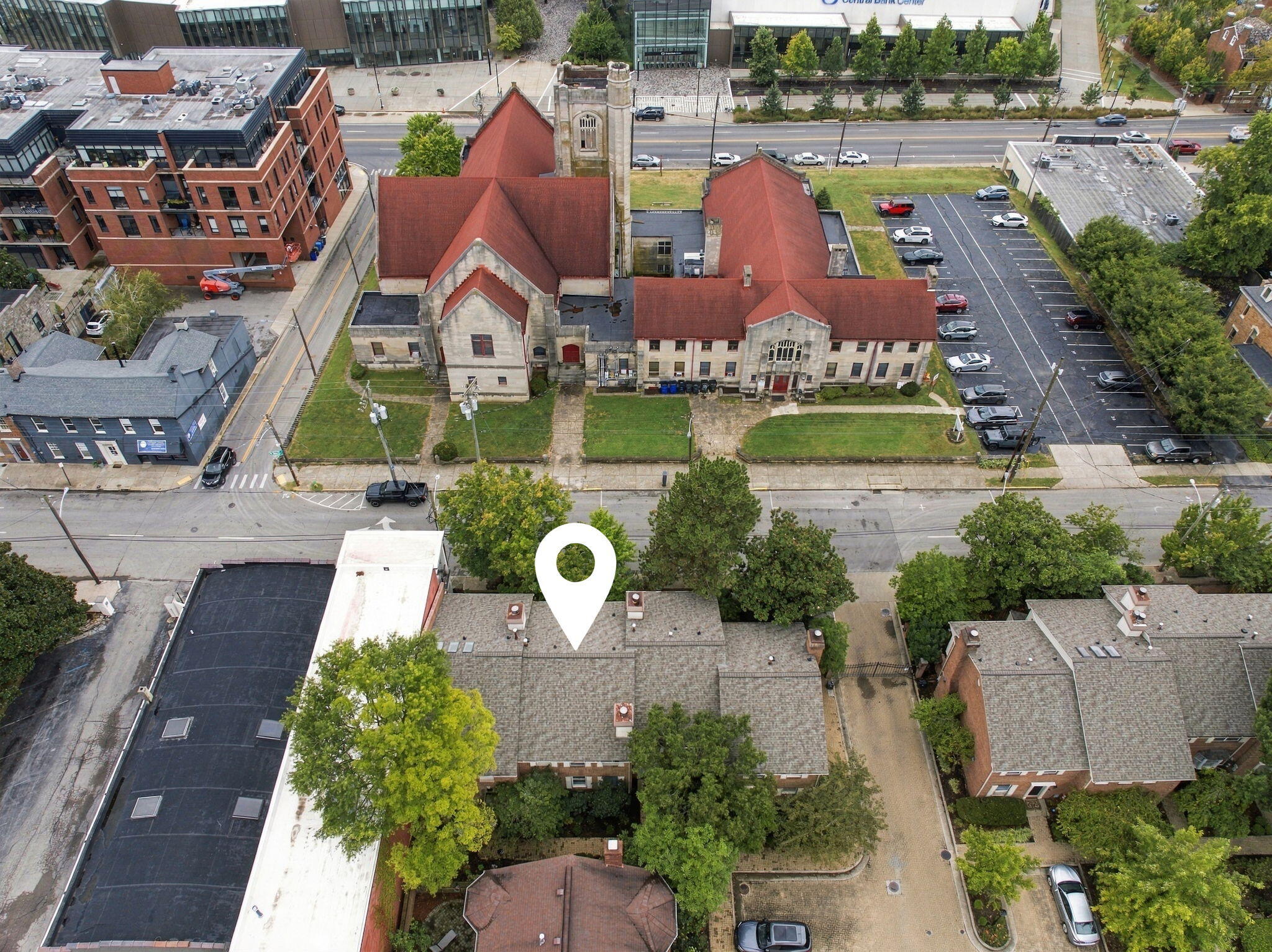 Aerial view of a downtown rooftop marked by a white location pin, across from a red-roofed stone building.