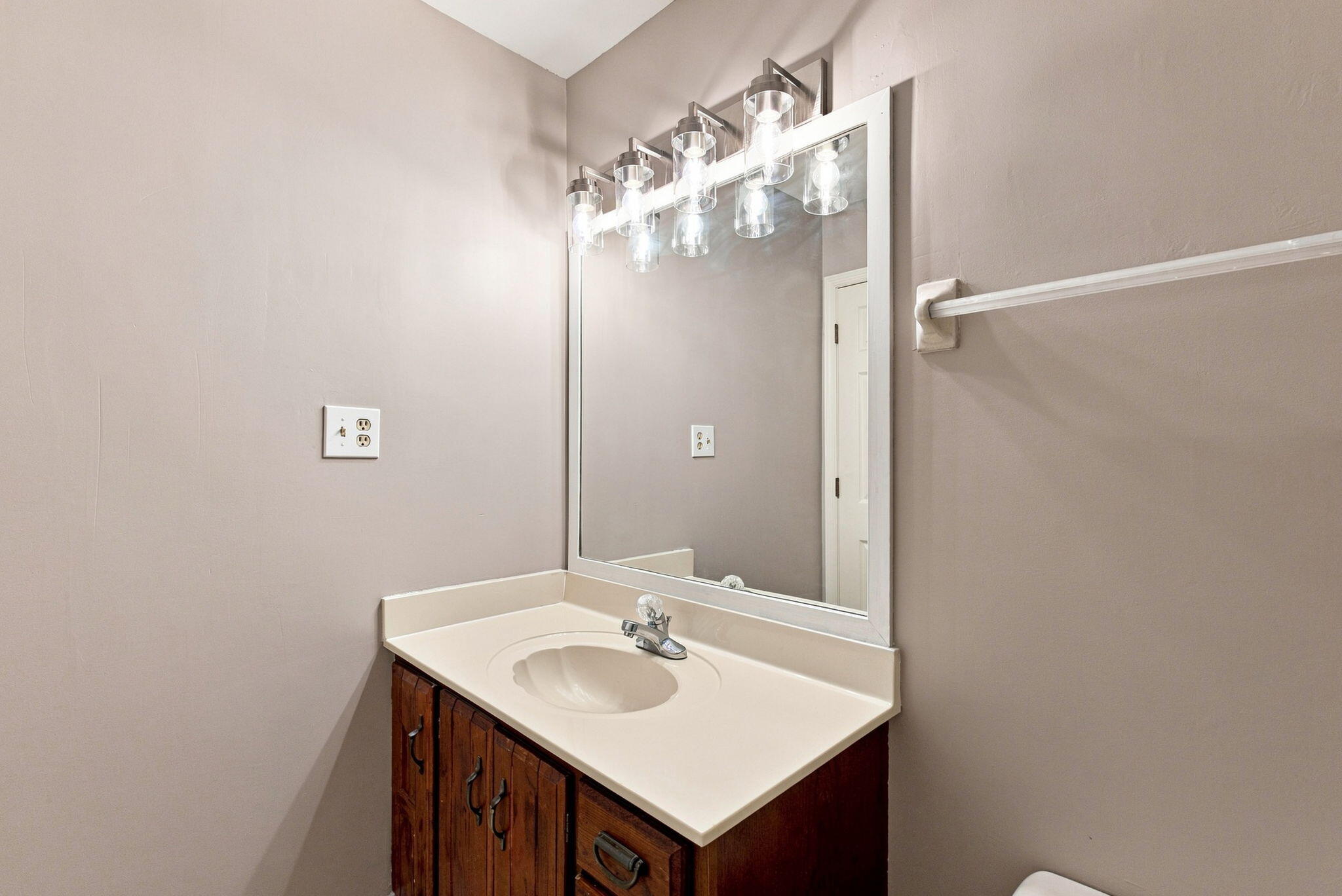 Bathroom vanity with an oval sink, dark wood cabinets, large mirror, and bright vanity lights.