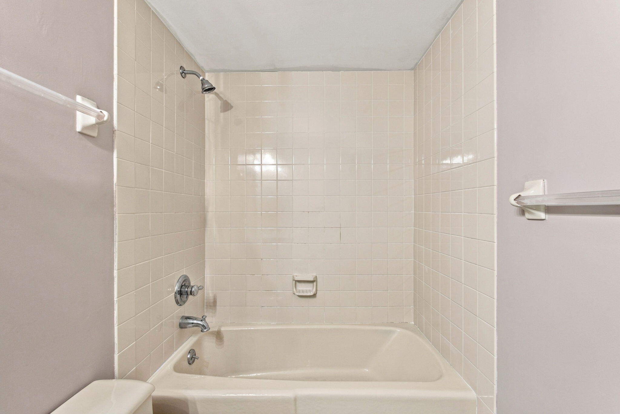 Bathroom tub with cream tile surround, showerhead, and grab bars.