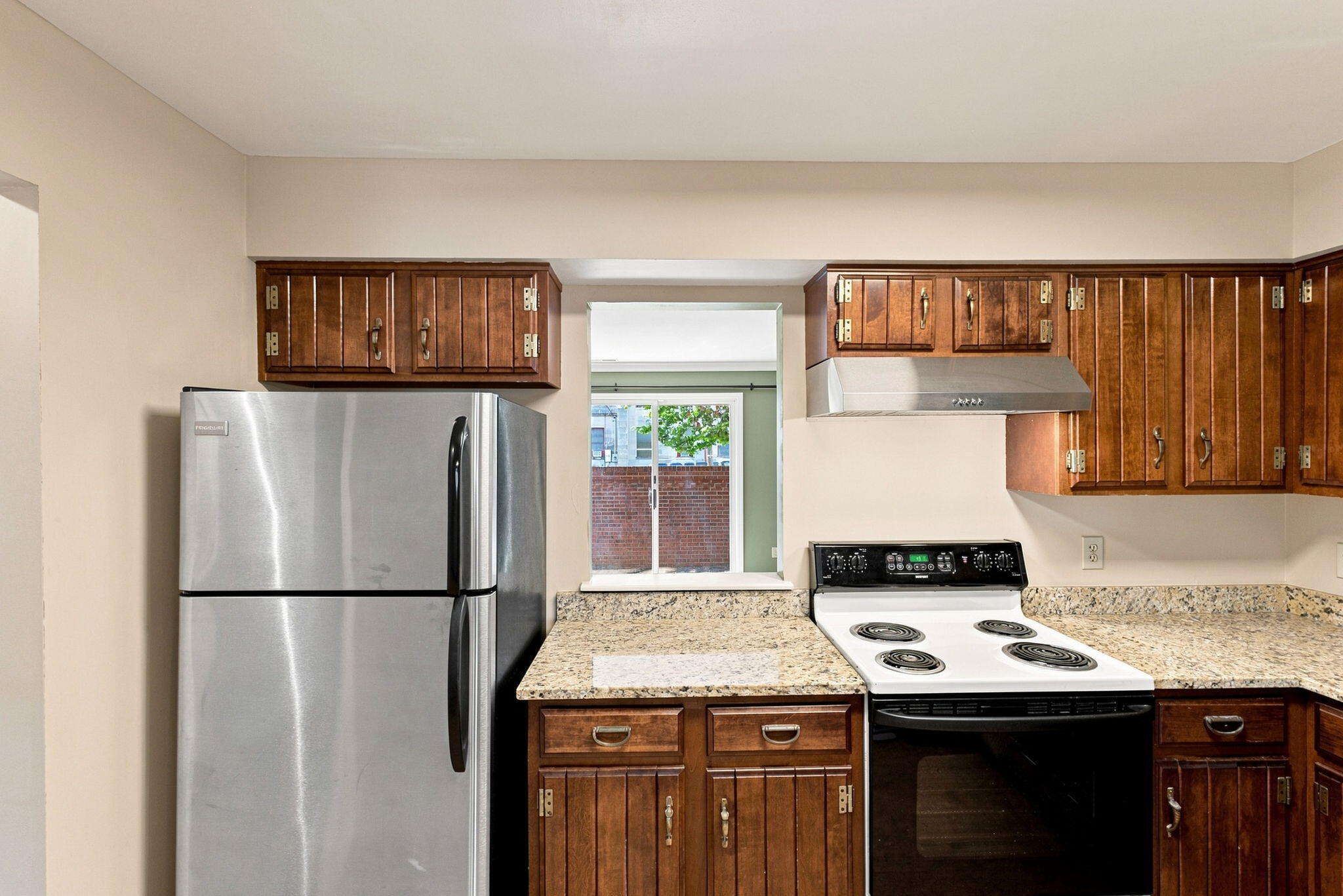 Kitchen with dark wood cabinets, granite countertops, and stainless steel refrigerator beside an electric range.