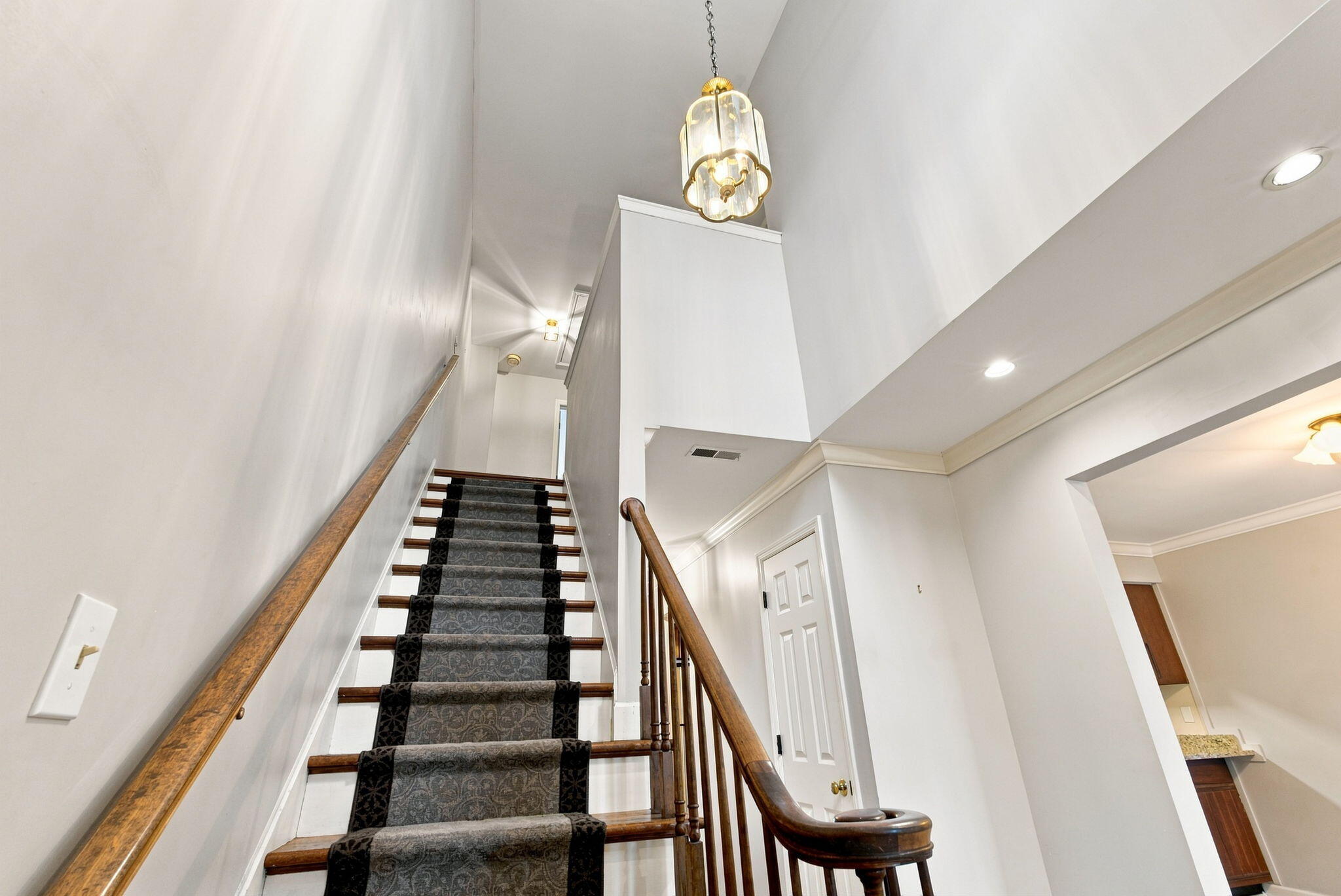Tall stairwell with a patterned carpet runner, dark wood railing, and brass-and-glass pendant light.