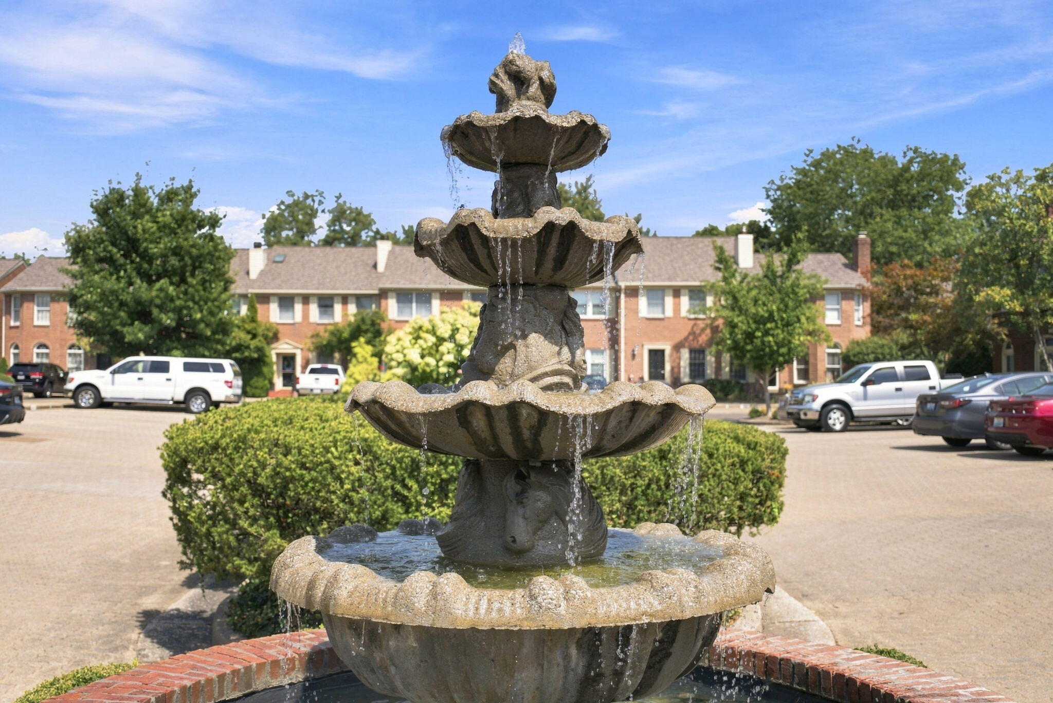 Tiered stone fountain in a landscaped courtyard in front of brick townhomes.