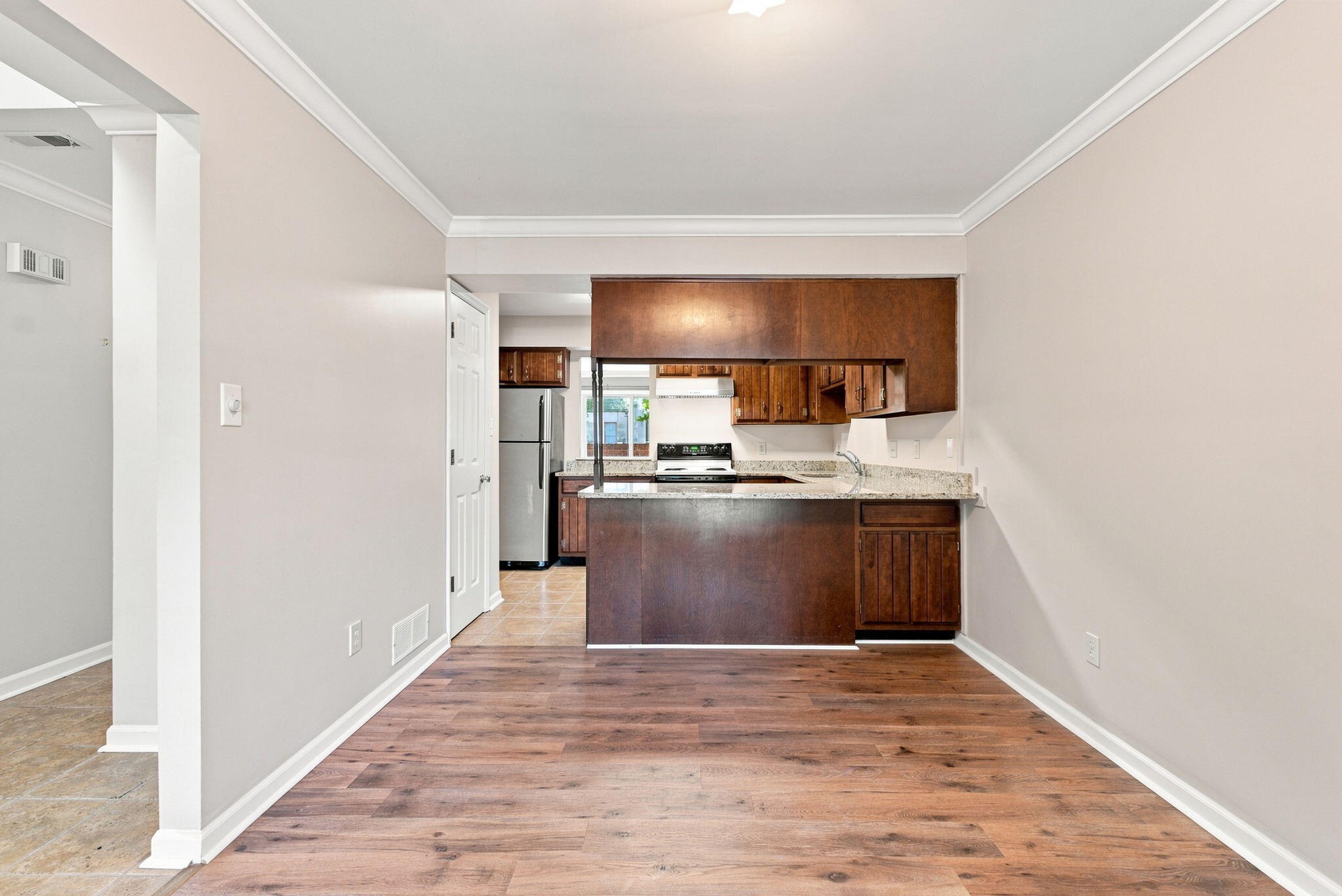 Unfurnished dining area overlooking a kitchen with dark wood cabinets and a granite peninsula.