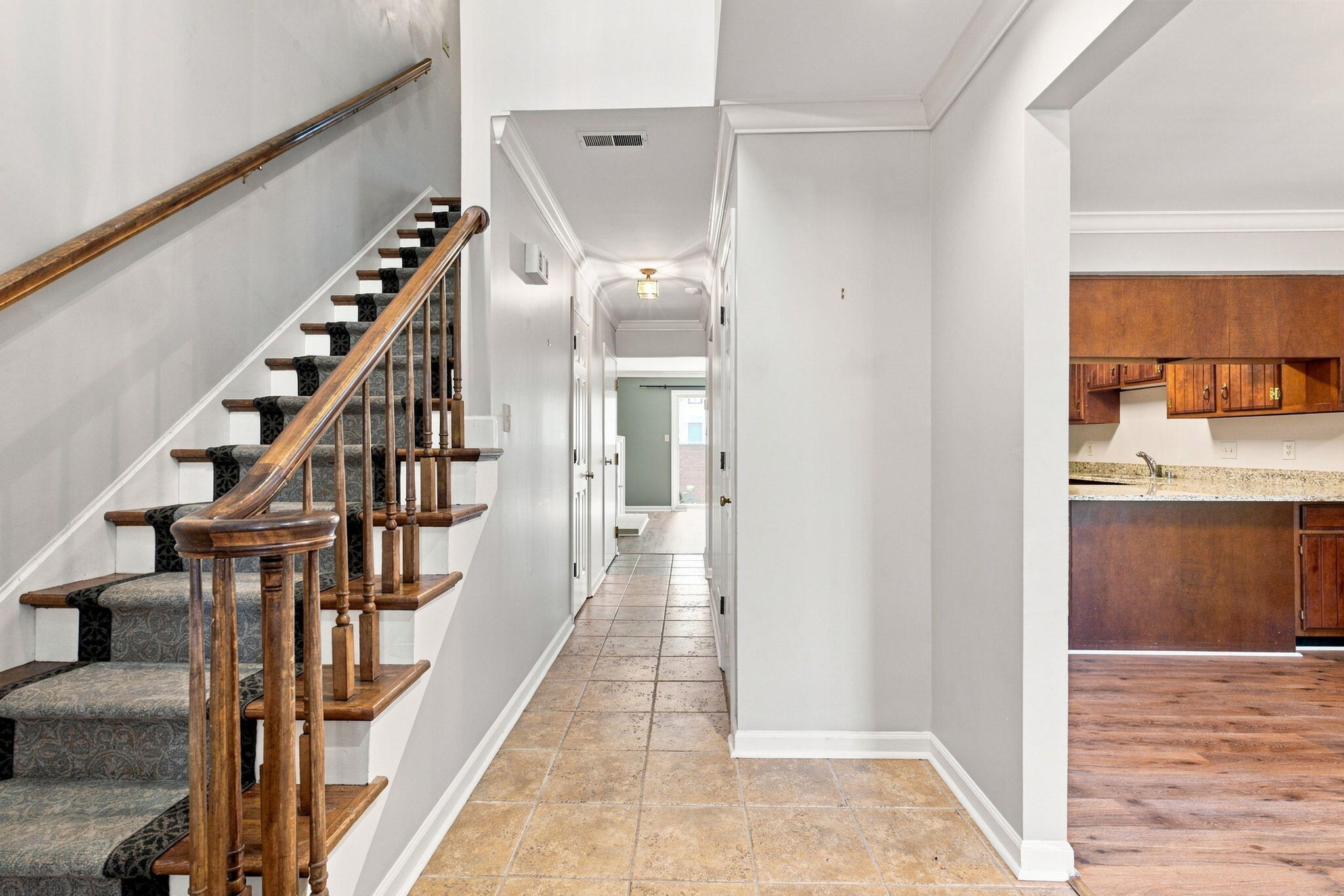Entry hall with a tiled floor, wooden staircase railings, and a glimpse of the kitchen.