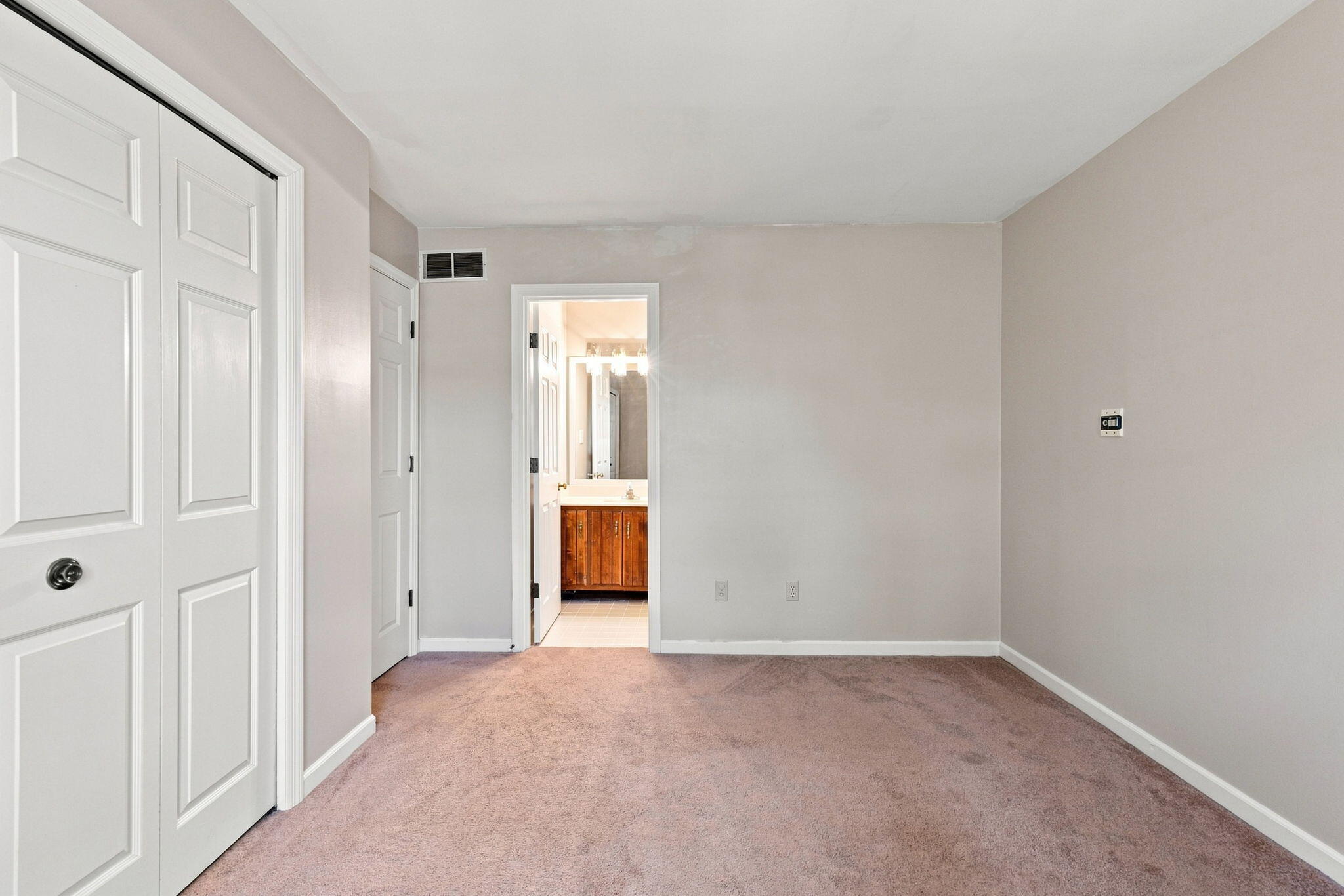 Empty carpeted bedroom with paneled closet doors and an open doorway to a bathroom.