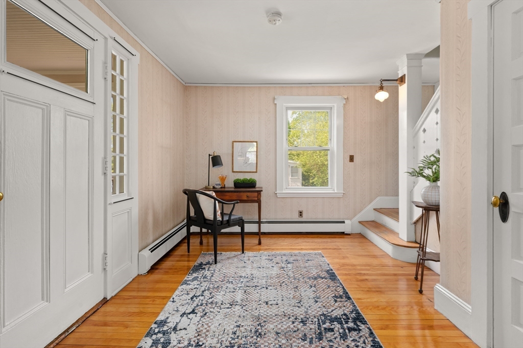 Entry hall with peach patterned walls, polished hardwood floors, a small desk, and a staircase.