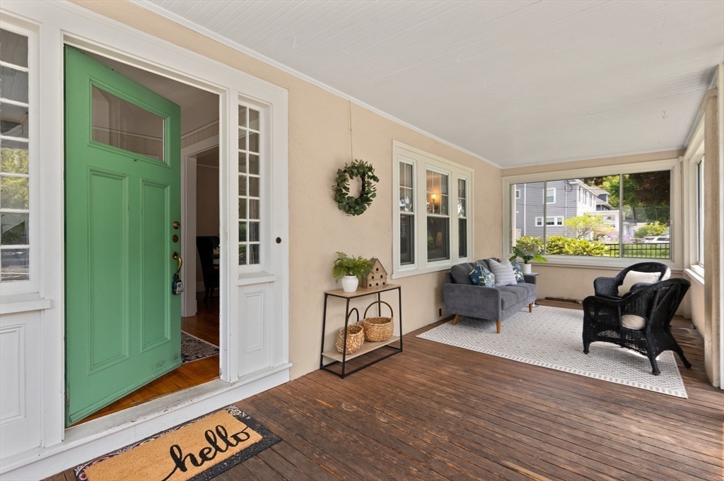 Enclosed front porch with a green door, gray loveseat, wicker chairs, and wood plank flooring.