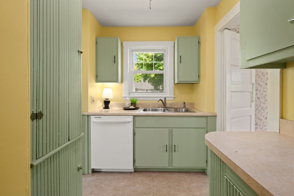 Kitchen with pale green cabinets, yellow walls, and a double-basin sink beneath the window.
