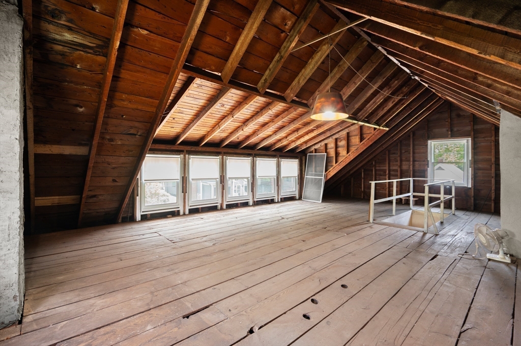 Unfinished attic with exposed wooden rafters, plank flooring, and a row of windows.